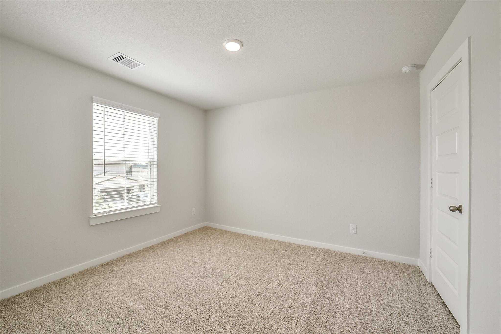Bright empty bedroom with light gray walls, beige carpet, window blinds in Davidson Homes The Trinity F, Magnolia, Texas