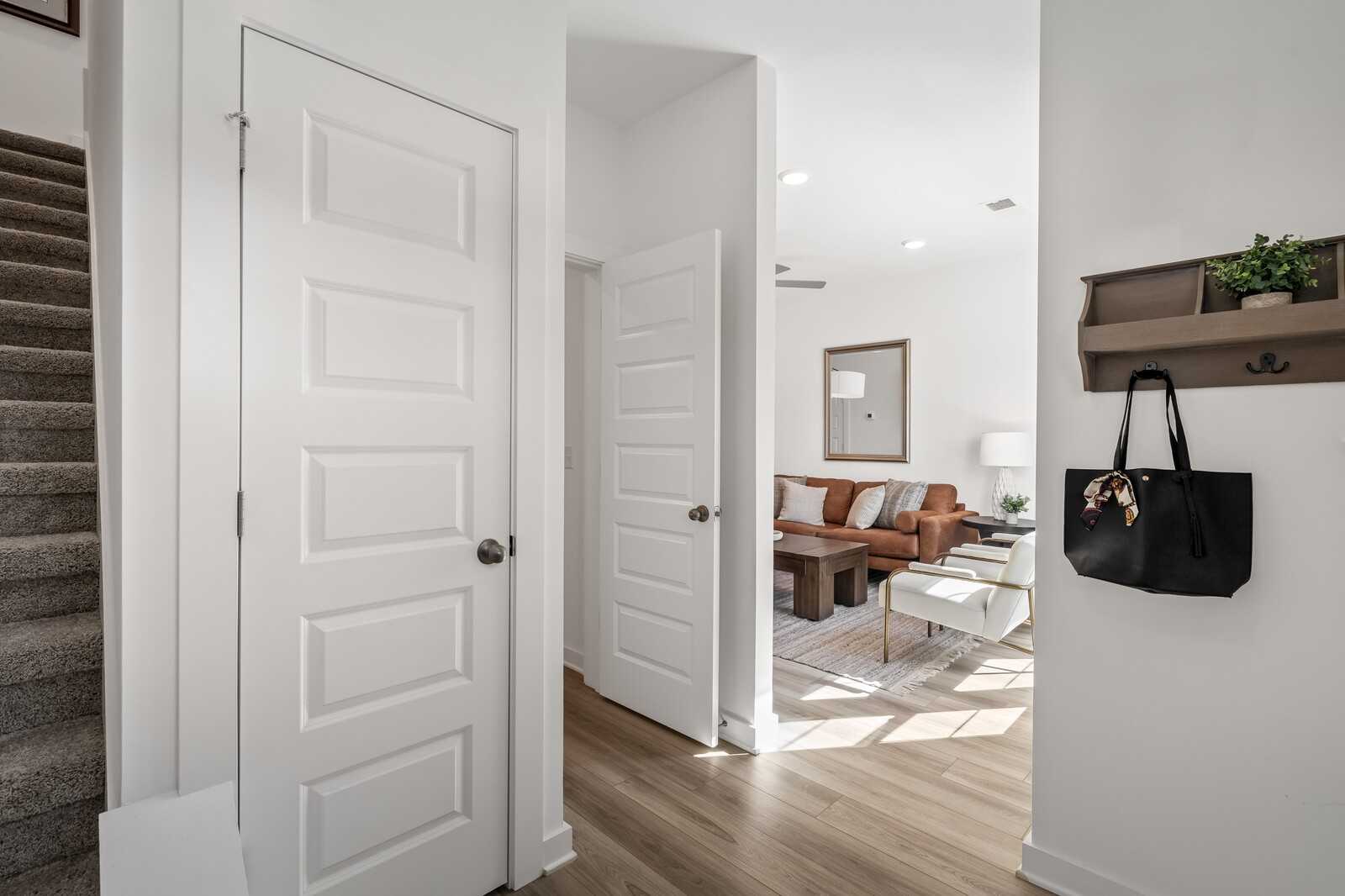 Bright entryway with white doors, hardwood floors, leather sofa, and stairs in Davidson Homes Cumberland B, Gallatin, TN