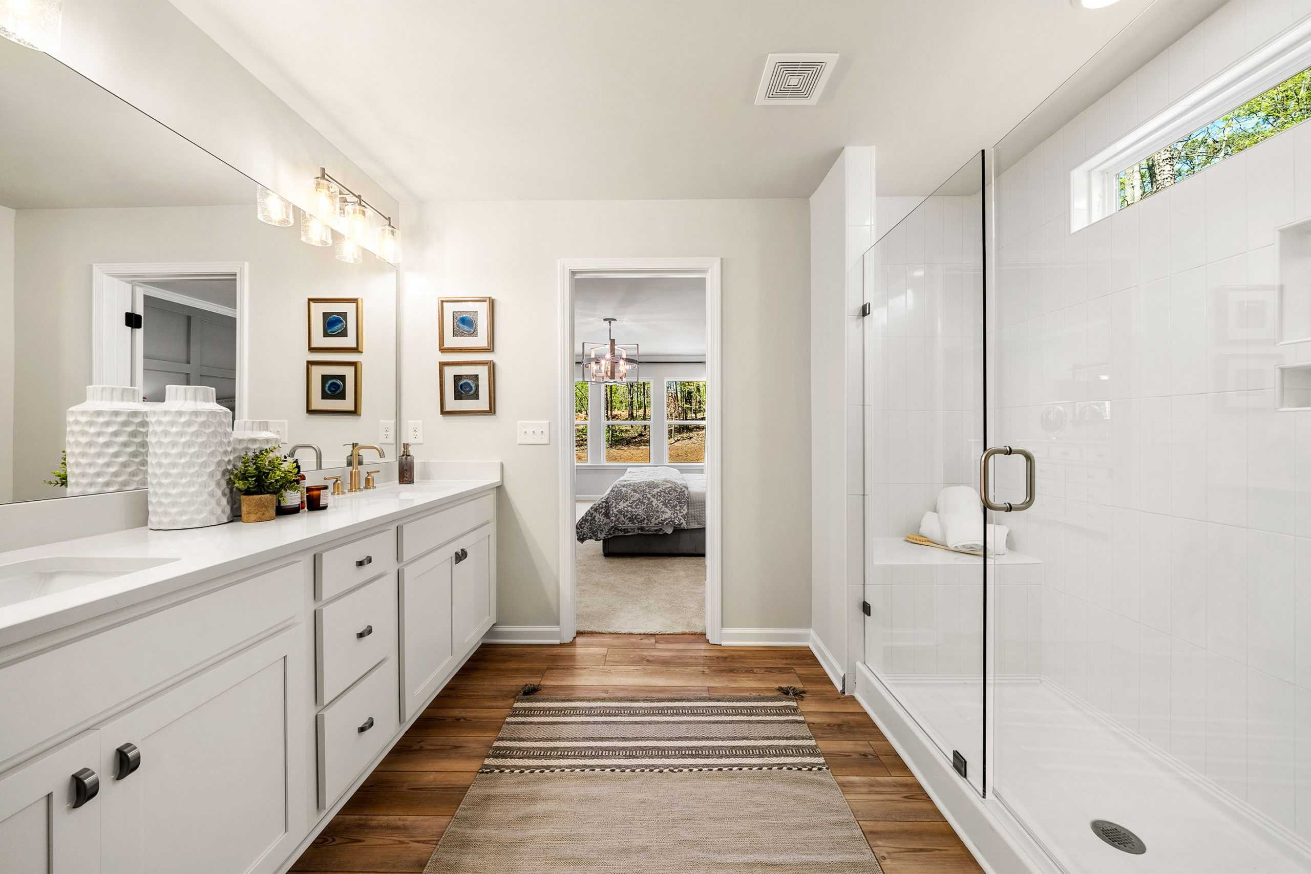 Spacious primary bathroom at Riverwood in Dallas GA with double vanity, frameless glass shower, hardwood floors by Davidson Homes