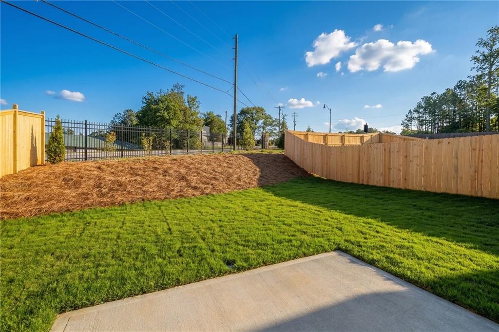 Private backyard with lush green lawn, wooden privacy fence, and concrete patio in The Gavin E, The Village at Shallowford, Kennesaw, Georgia