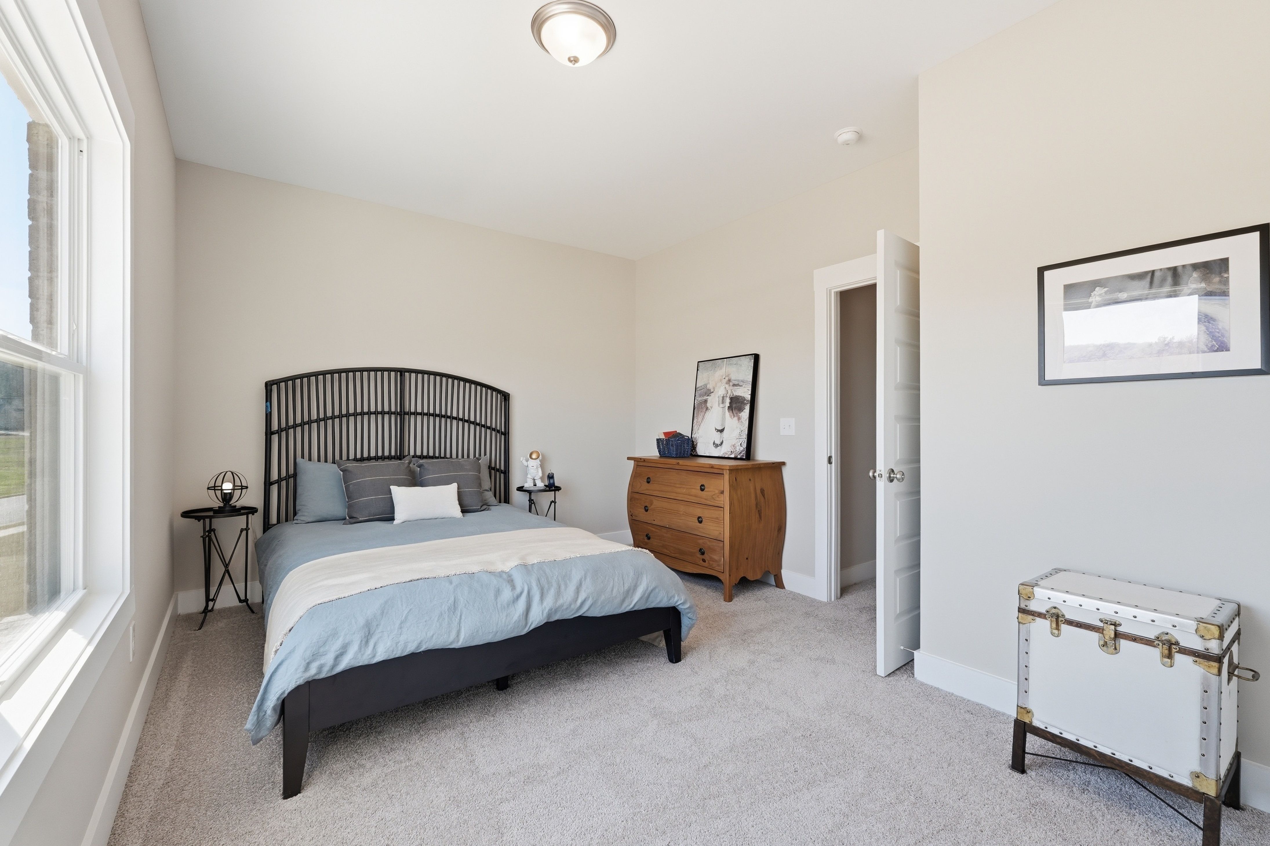Spacious bedroom at The Meadows at Hampton Cove in Owens Cross Roads AL featuring black wrought iron headboard bed, beige walls, and wooden dresser