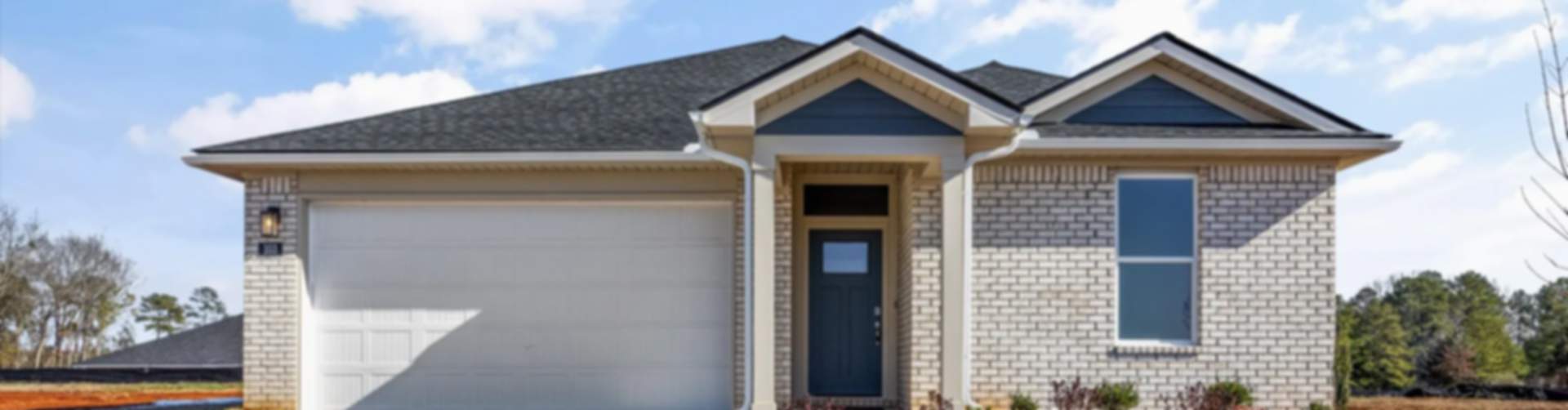 Front view of modern brick new construction home with white garage, blue entry door, and shrubs in Phenix City