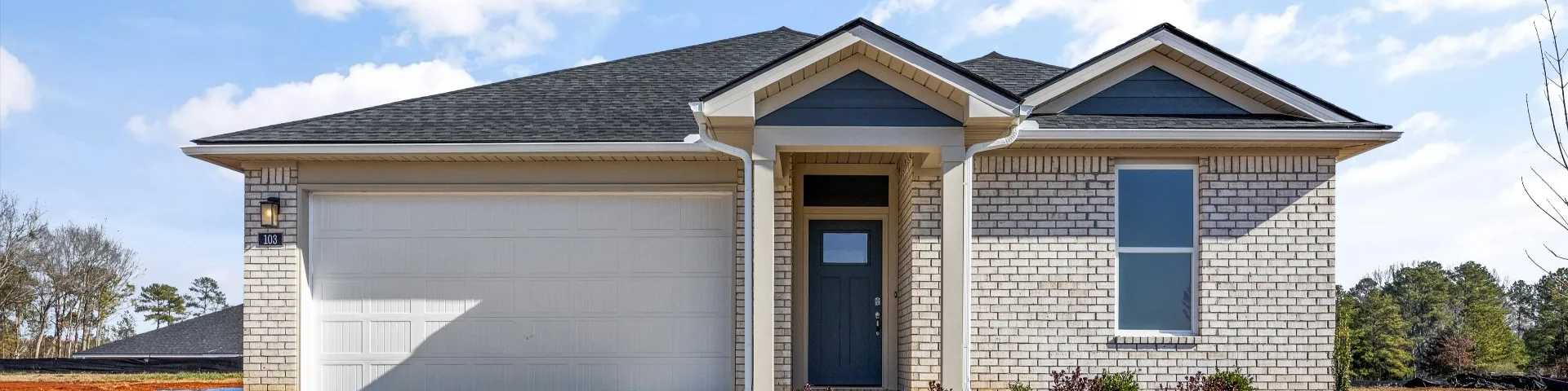 Front view of modern brick new construction home with white garage, blue entry door, and shrubs in Phenix City