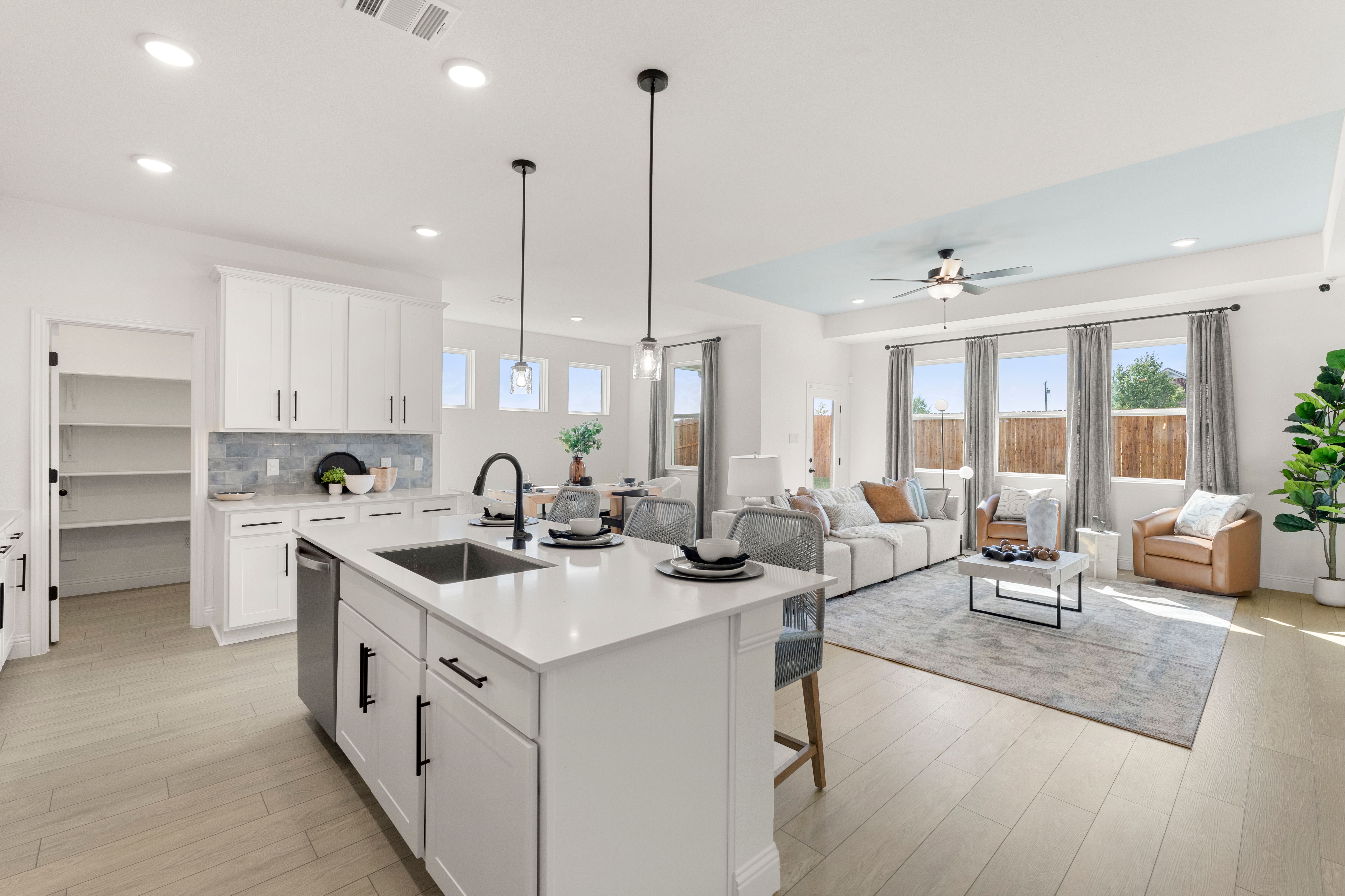 Spacious open-concept kitchen and living room in The Laurel home with white island, stainless sink, gray sofa, and natural light