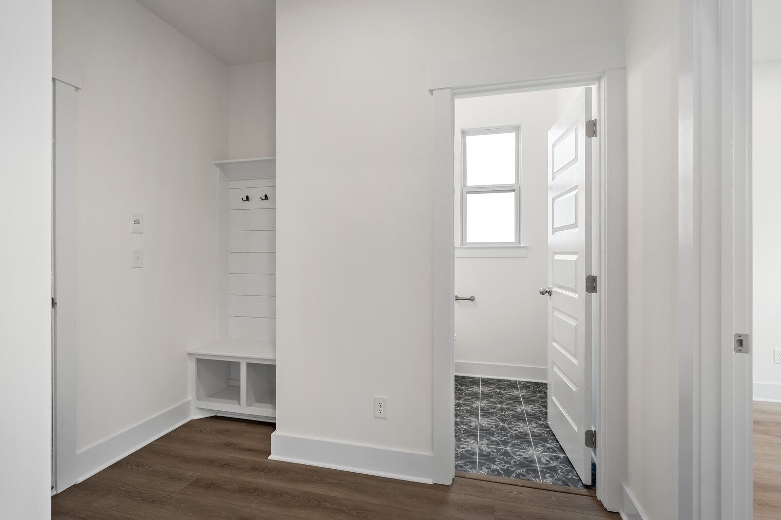 Bright mudroom with built-in bench, coat hooks, and white shiplap walls adjacent to powder room with patterned tile floor in Davidson Homes The Willow C, Gallatin TN