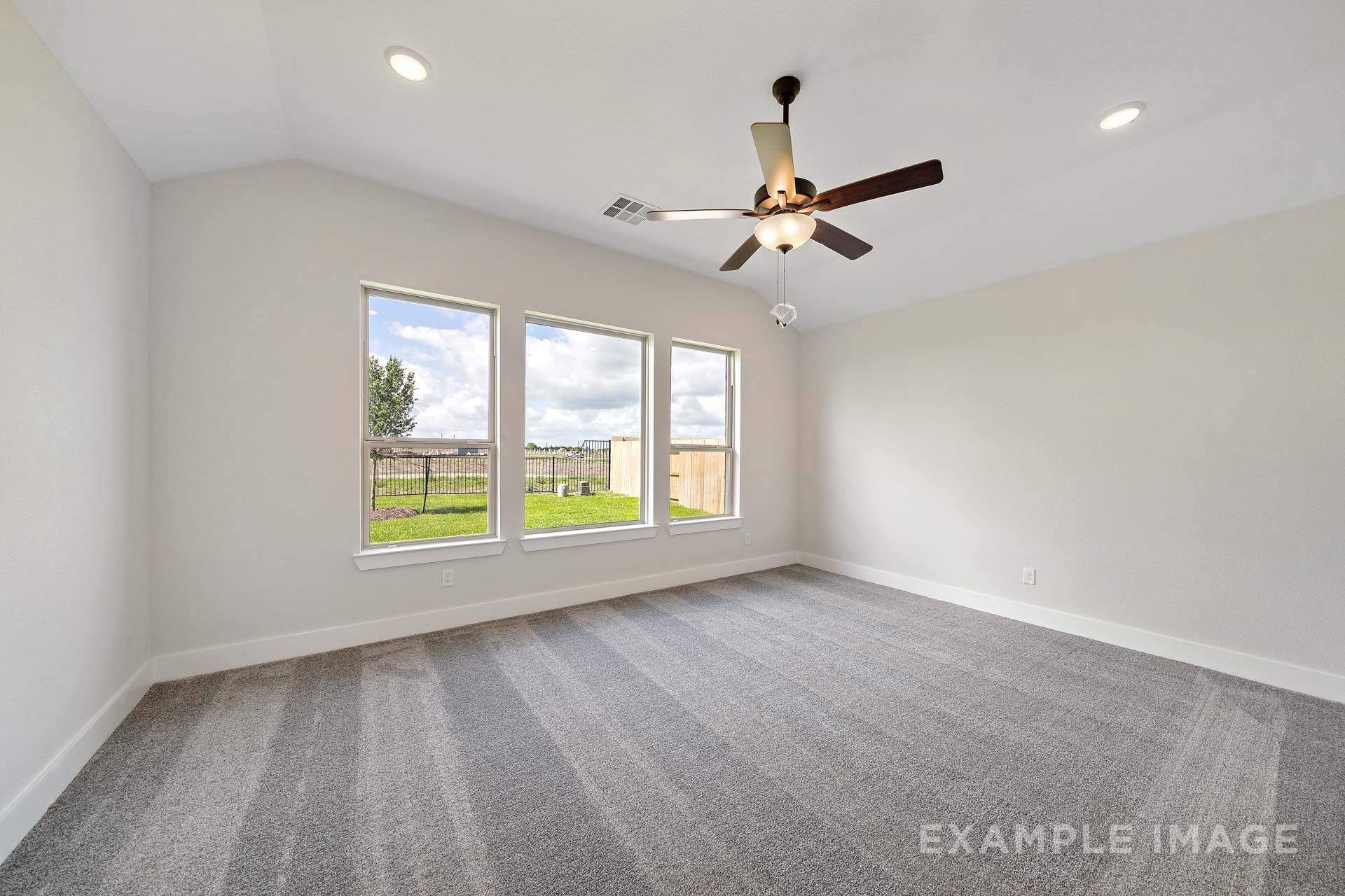 Spacious master suite in The Victoria by Davidson Homes with vaulted ceiling, ceiling fan, and backyard windows