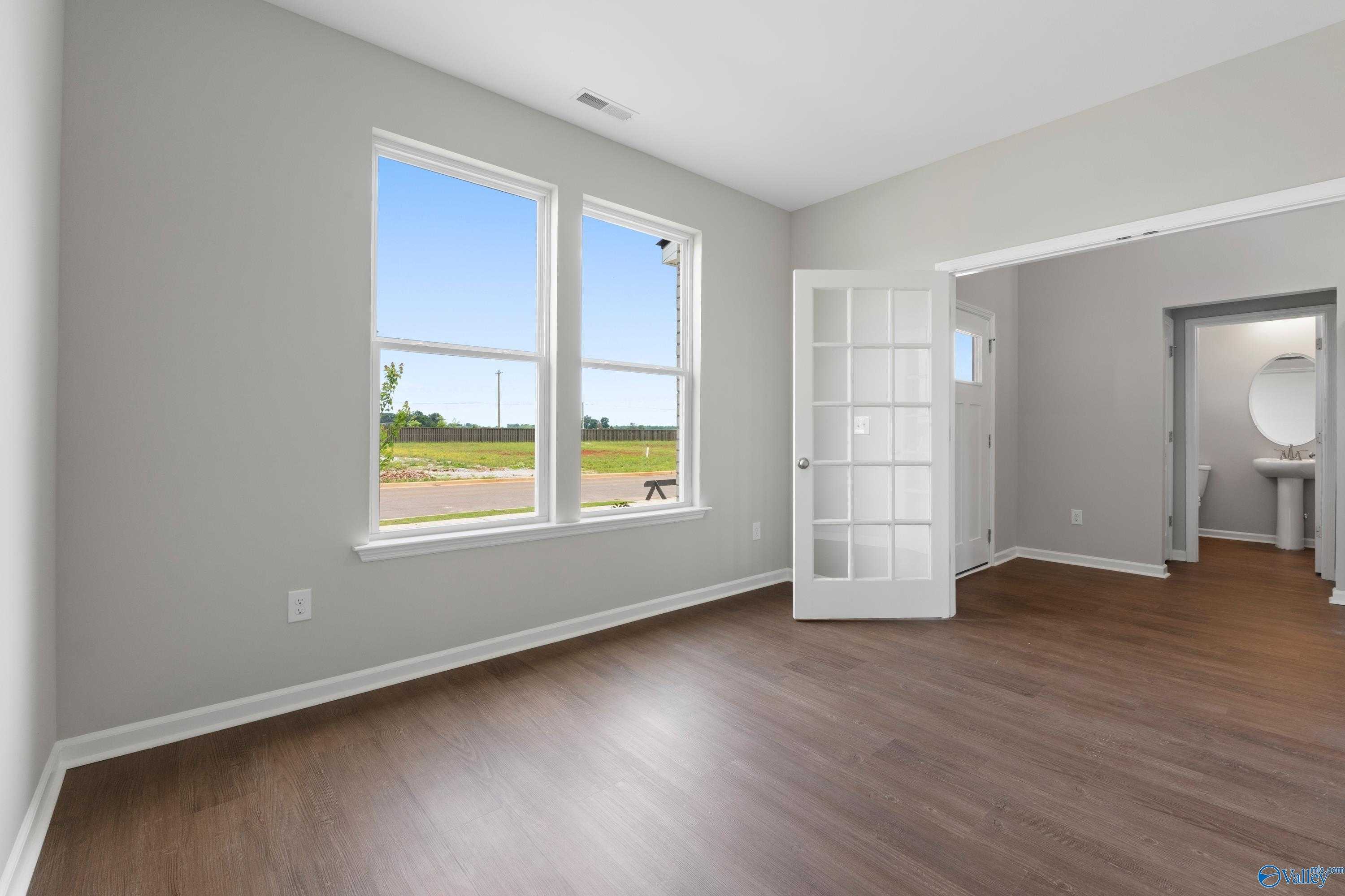 Bright living room with large windows overlooking fields, open French door to powder room, hardwood floors in Davidson Homes The Dorado, Athens AL