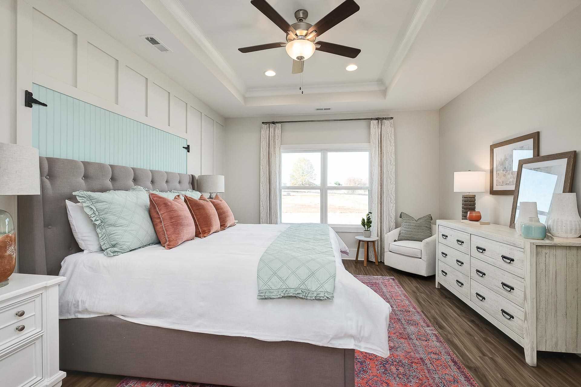Spacious master bedroom at Newby Chapel in Athens AL with tufted gray bed, teal pillows, hardwood floors, accent chair, and ceiling fan