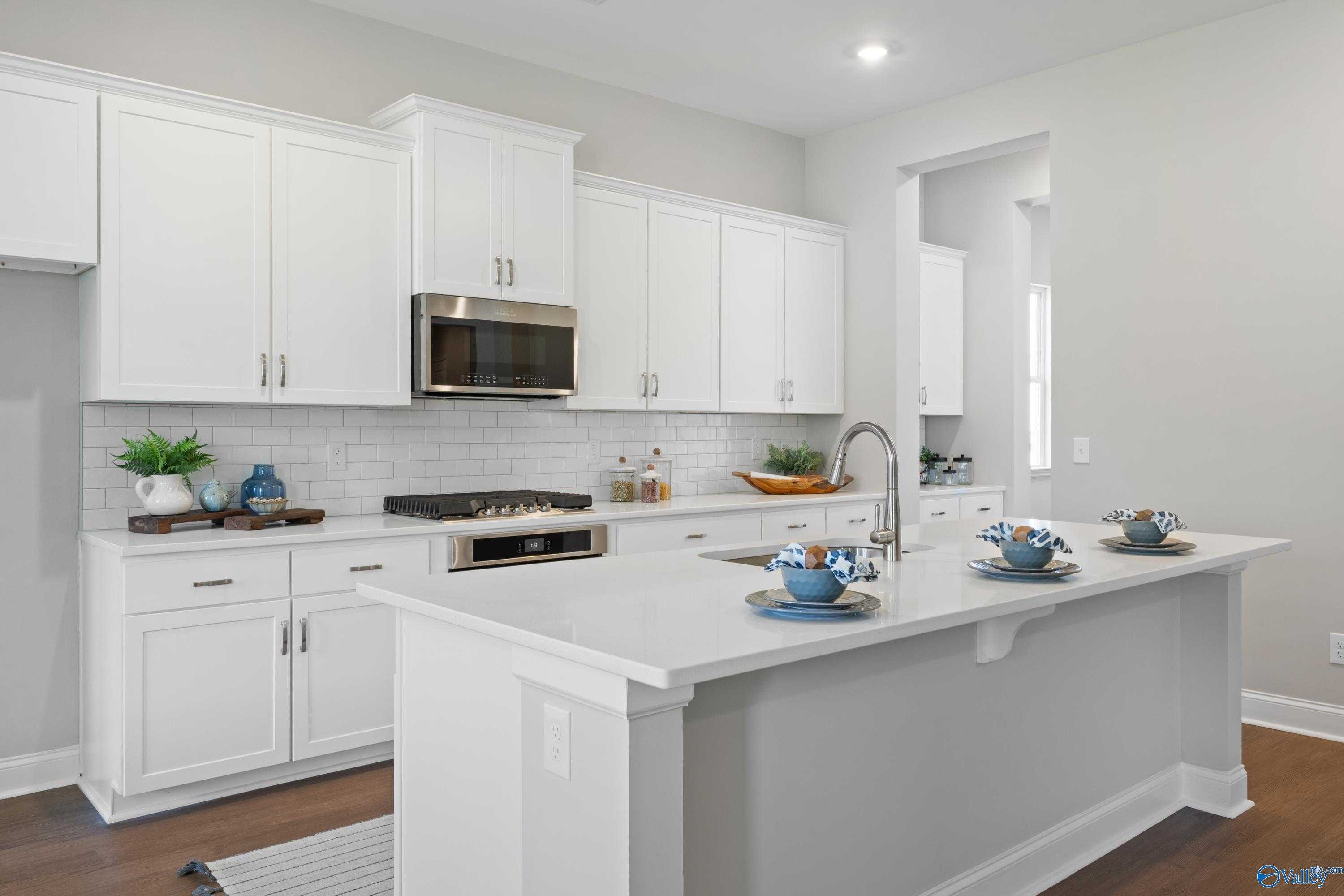 Modern white kitchen with shaker cabinets, stainless cooktop, subway tile backsplash, and large island in The Haven 5-bedroom home, Owens Cross Roads, AL