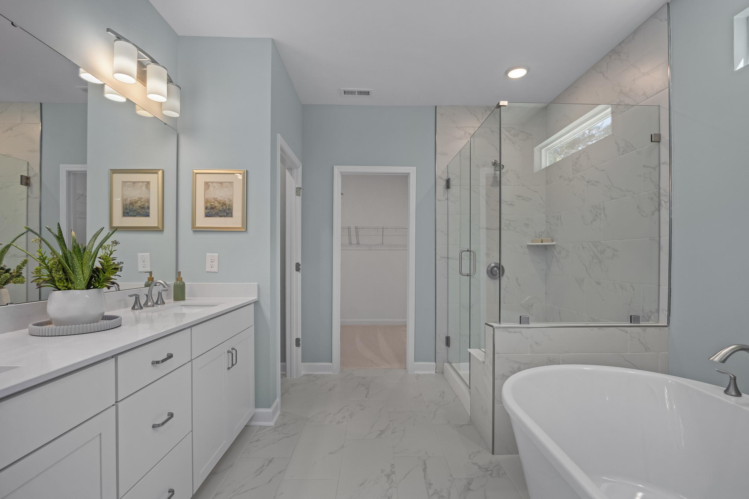 Spacious master bathroom in The Hickory II featuring freestanding tub, glass shower, white vanities, and marble tiles