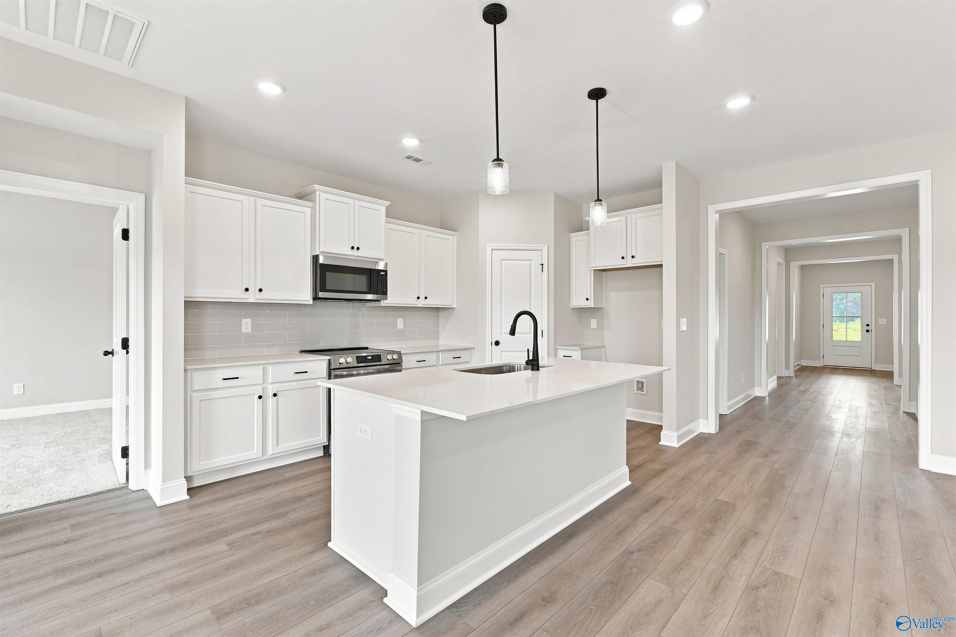 Bright white kitchen with large island, black faucet, pendant lights, and wood-look floors in Davidson Homes Everett B, Toney AL