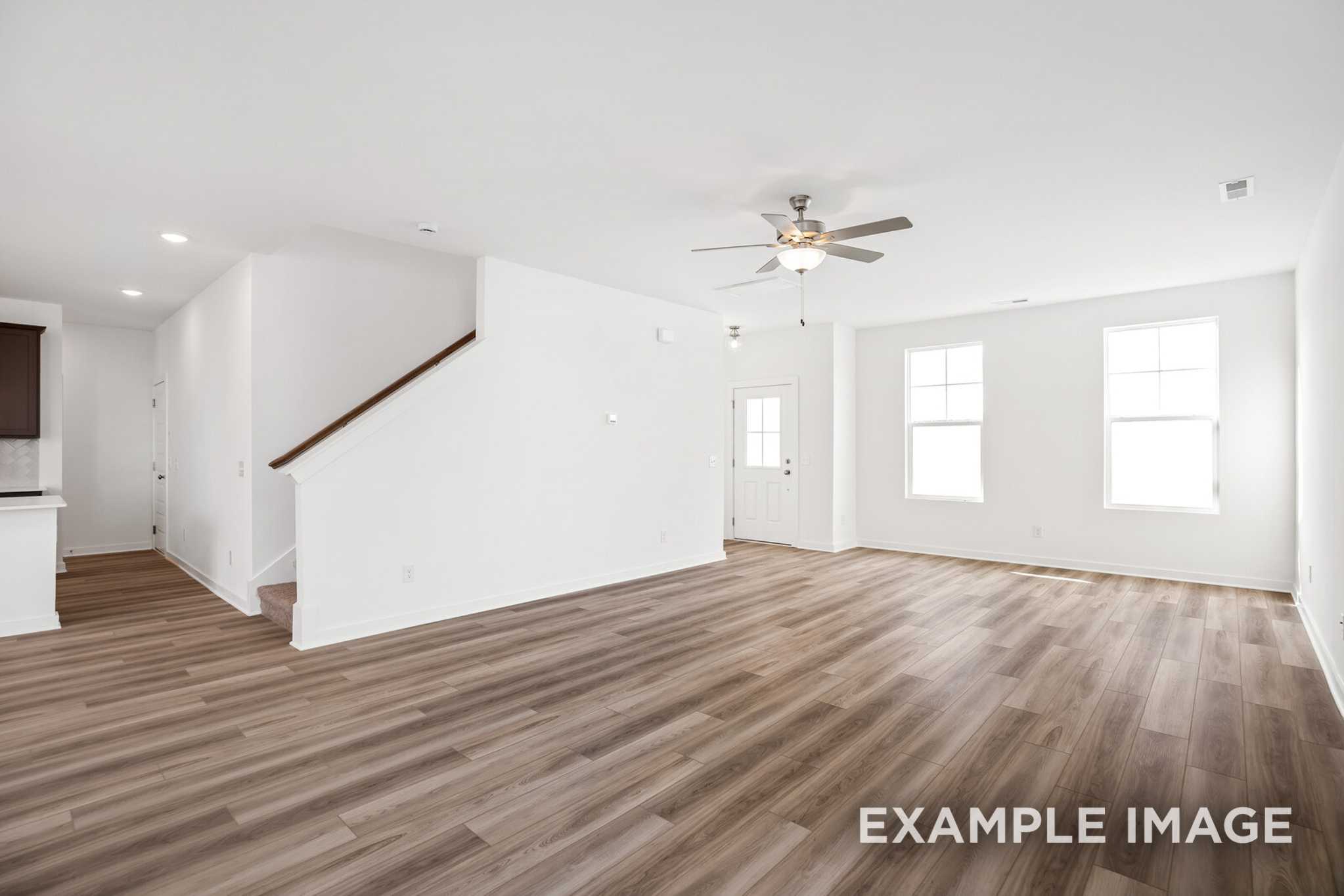 Spacious open-concept living area in The Murray B with hardwood floors, ceiling fan, staircase, and large windows