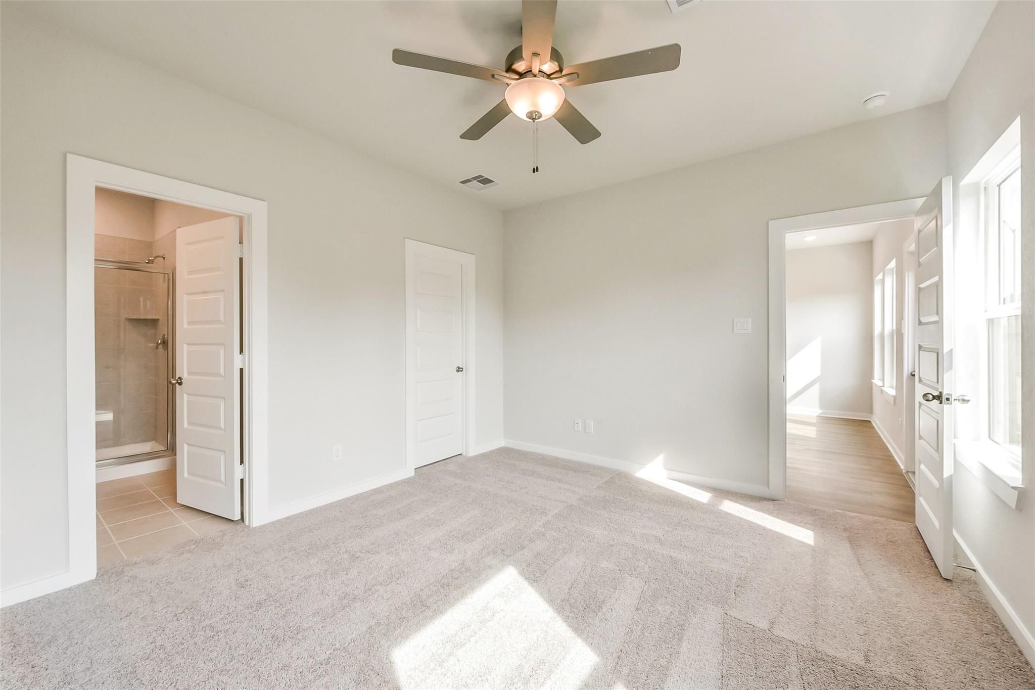 Spacious secondary bedroom with ceiling fan, carpet flooring, and en-suite bathroom in Davidson Homes The Comal G, Dayton, Texas
