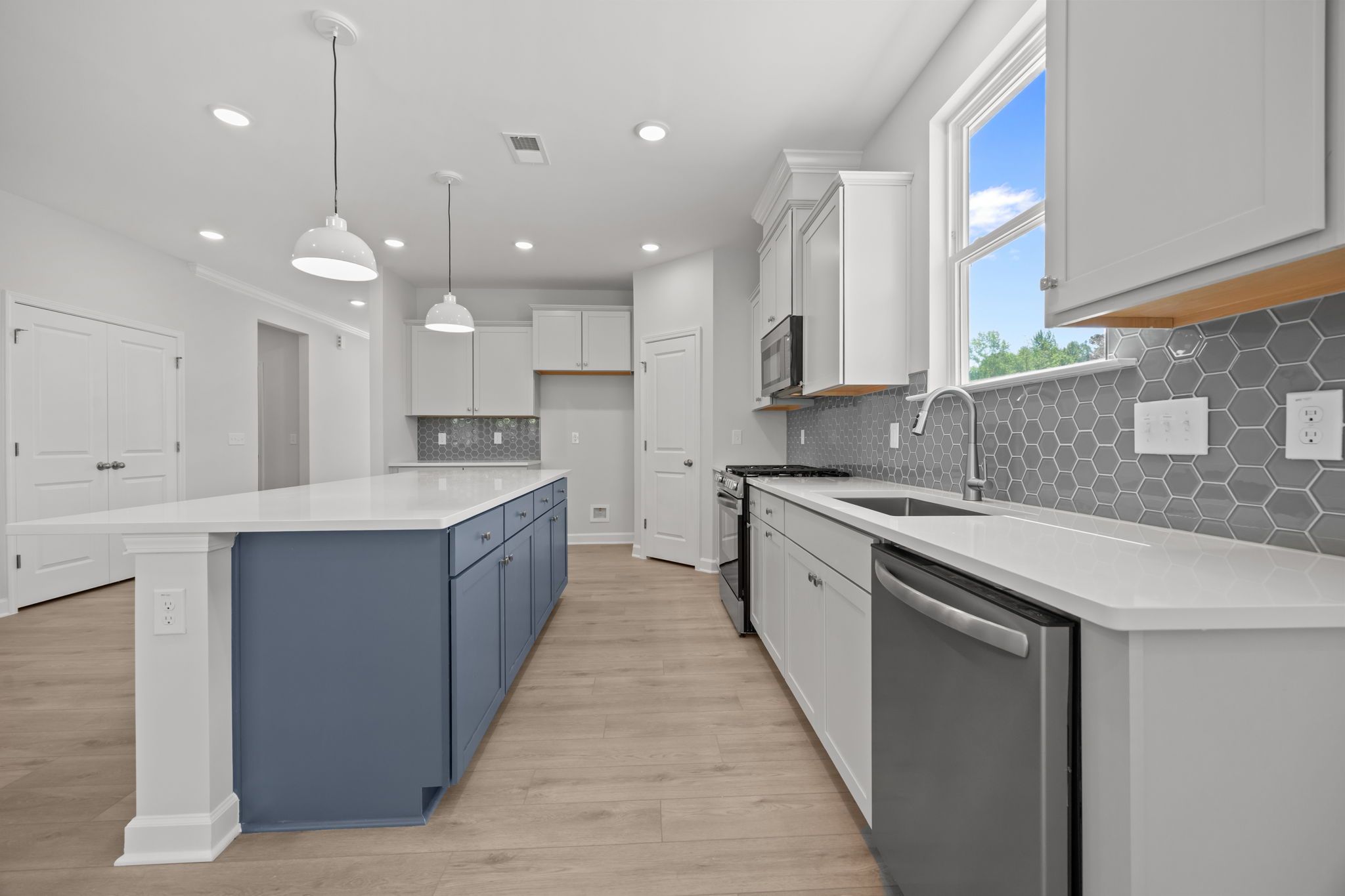 Modern kitchen in The Ashport B featuring a blue center island, white cabinetry, quartz countertops, and gray tile backsplash.
