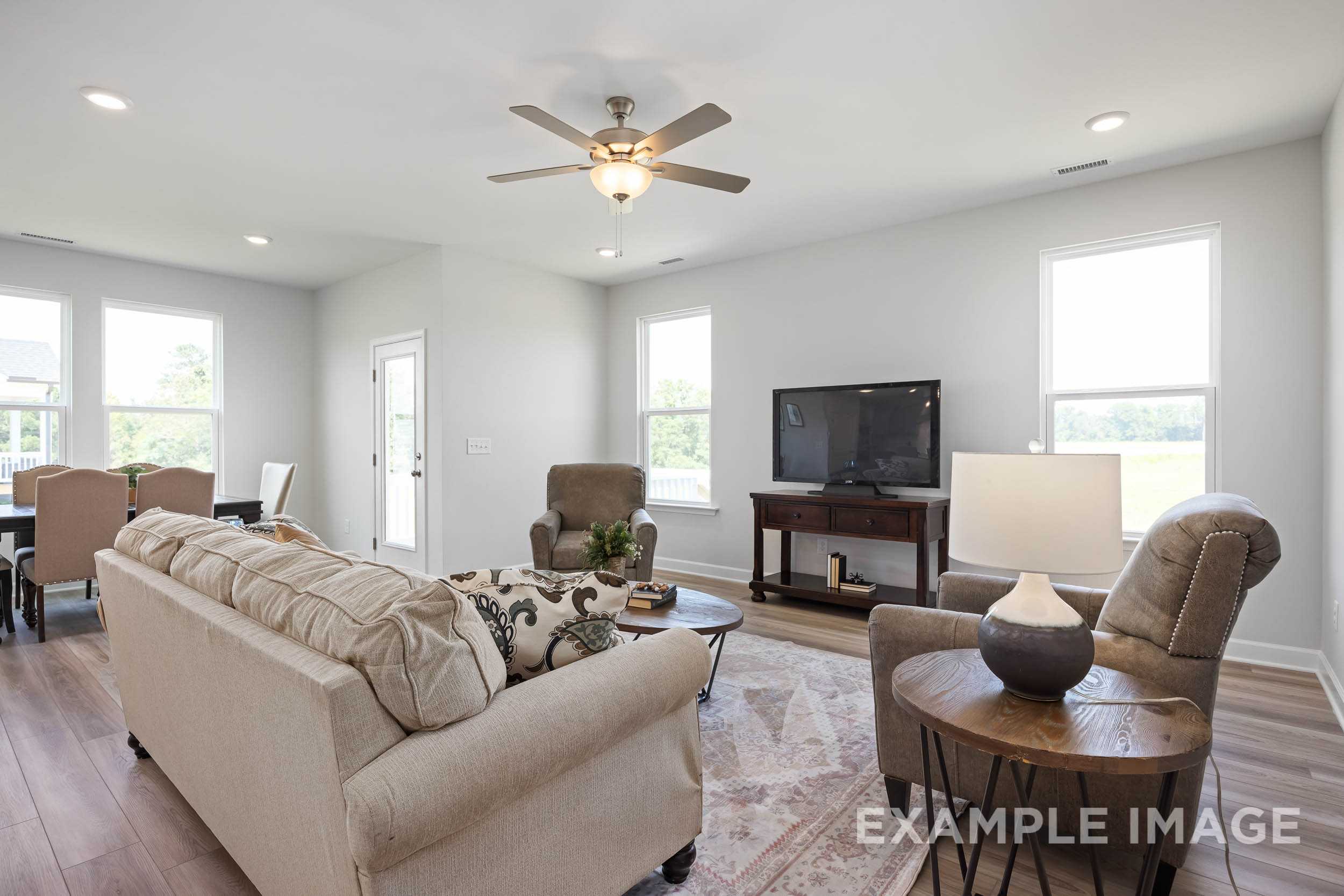Spacious living room in The Daphne C with beige sofas, ceiling fan, TV console, large windows, and hardwood floors