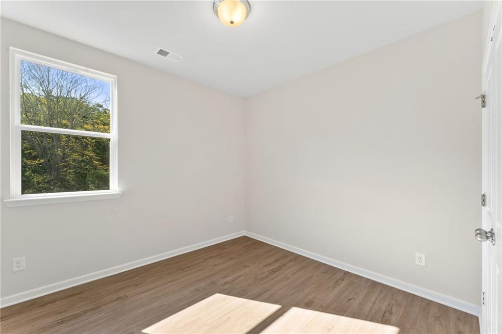 Bright secondary bedroom with beige walls, large window overlooking trees, hardwood floors in Davidson Homes The Willow B, Dallas, Georgia