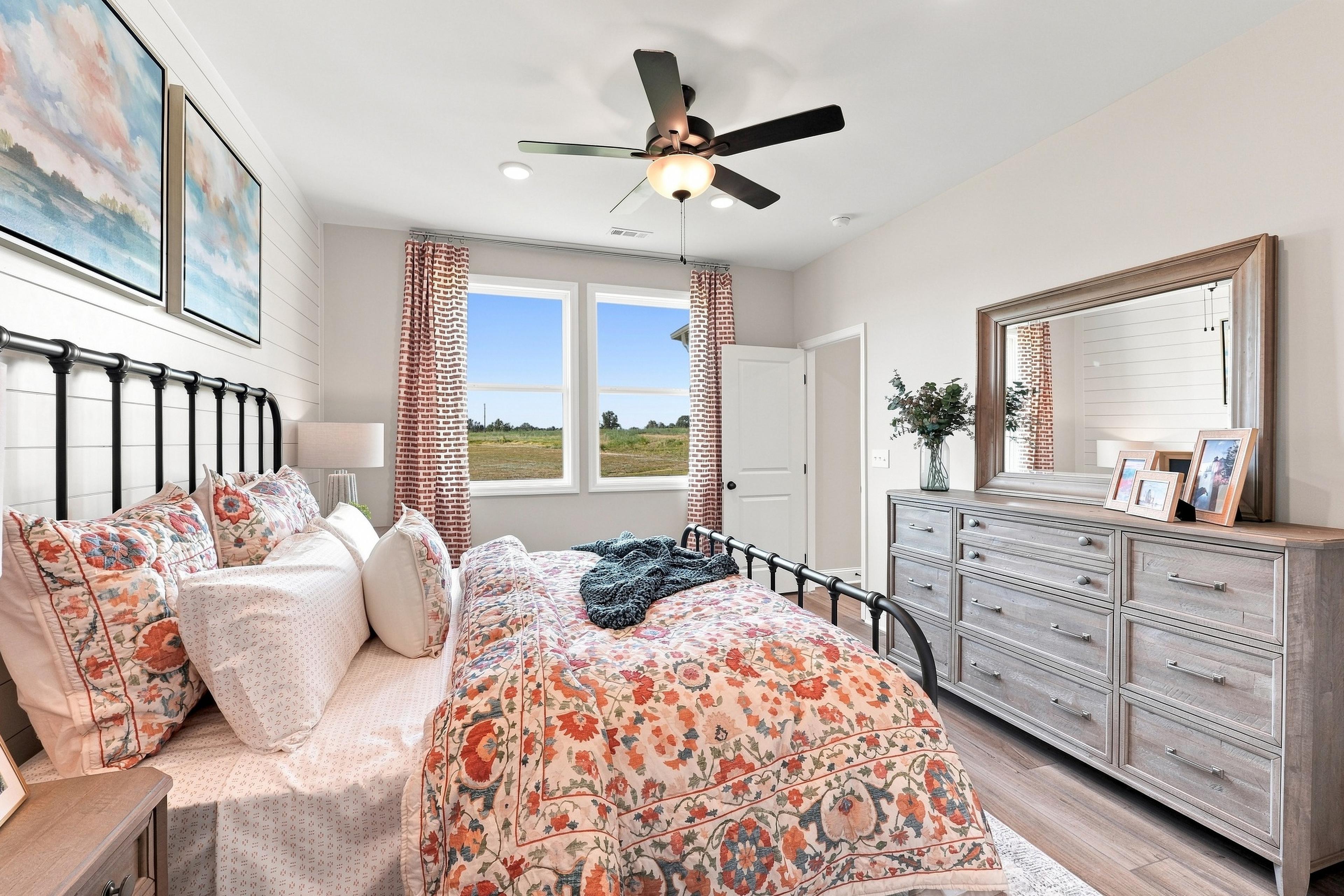 Primary bedroom at Bailey Park in Fayetteville, TN by Davidson Homes with black metal bed, floral bedding, and dresser with mirror