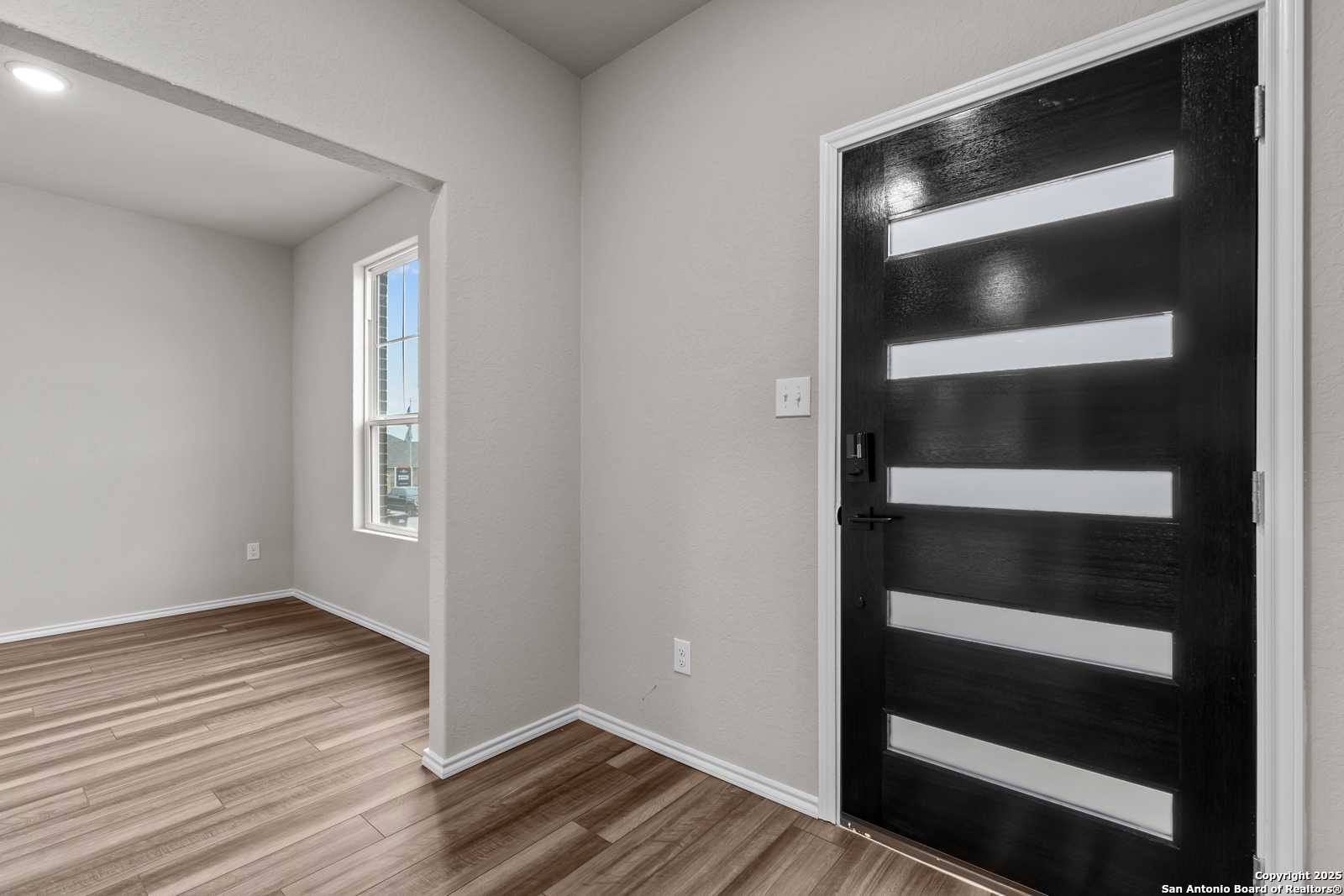 Contemporary bedroom entry with modern black frosted glass door, hardwood floors, and window in Davidson Homes The Murray I, San Antonio