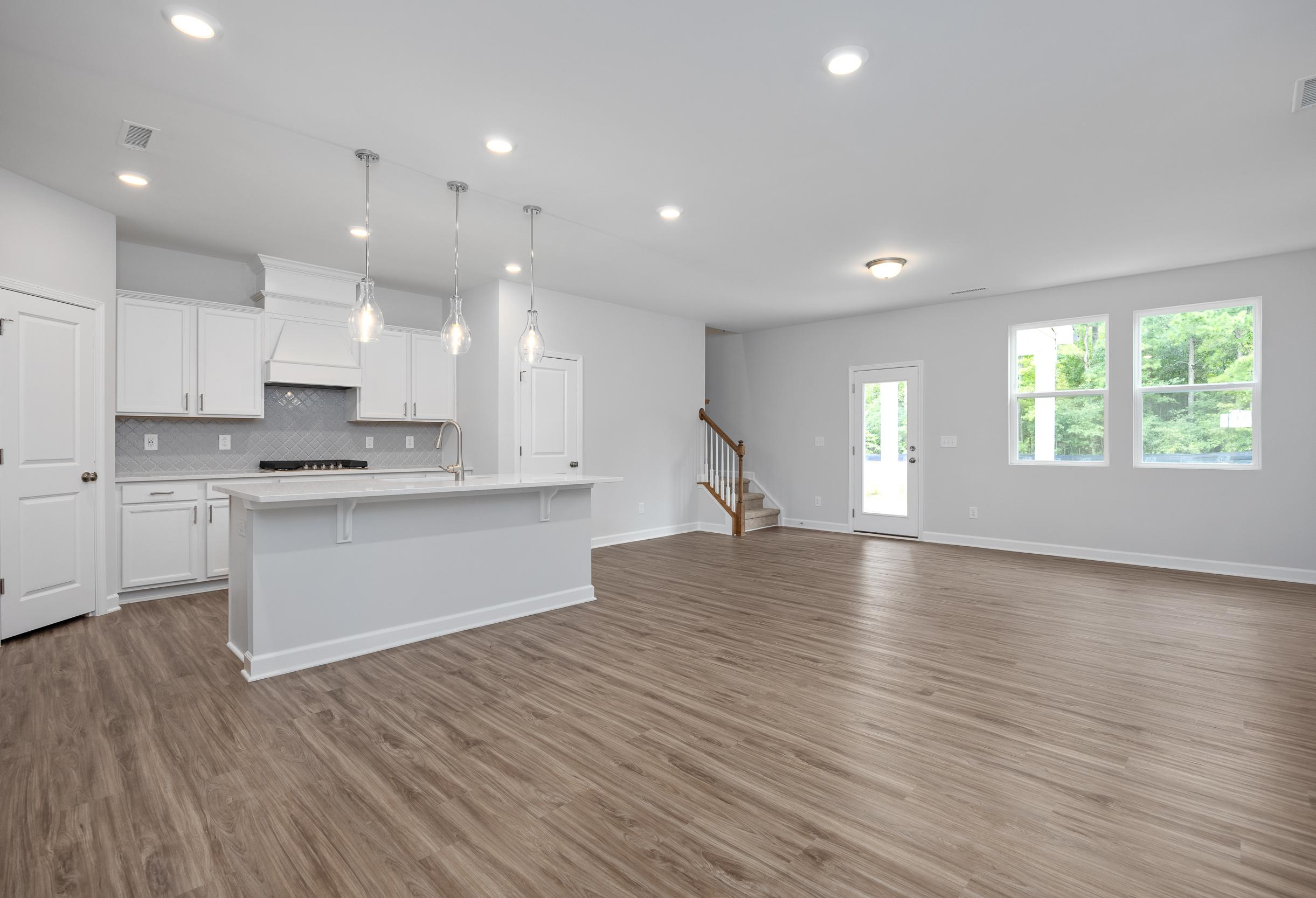 Open-concept kitchen and living area in The Durham featuring white cabinetry, a spacious island, and wood-style flooring.