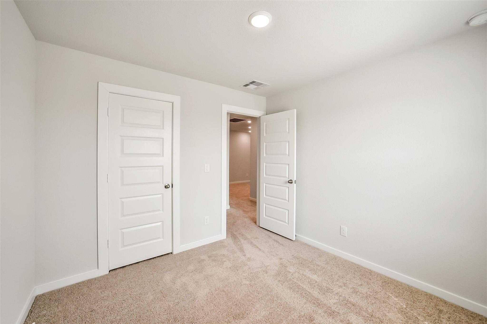 Spacious secondary bedroom with neutral beige walls, tan carpet, and double white doors in Davidson Homes The Blanco E, Magnolia, Texas
