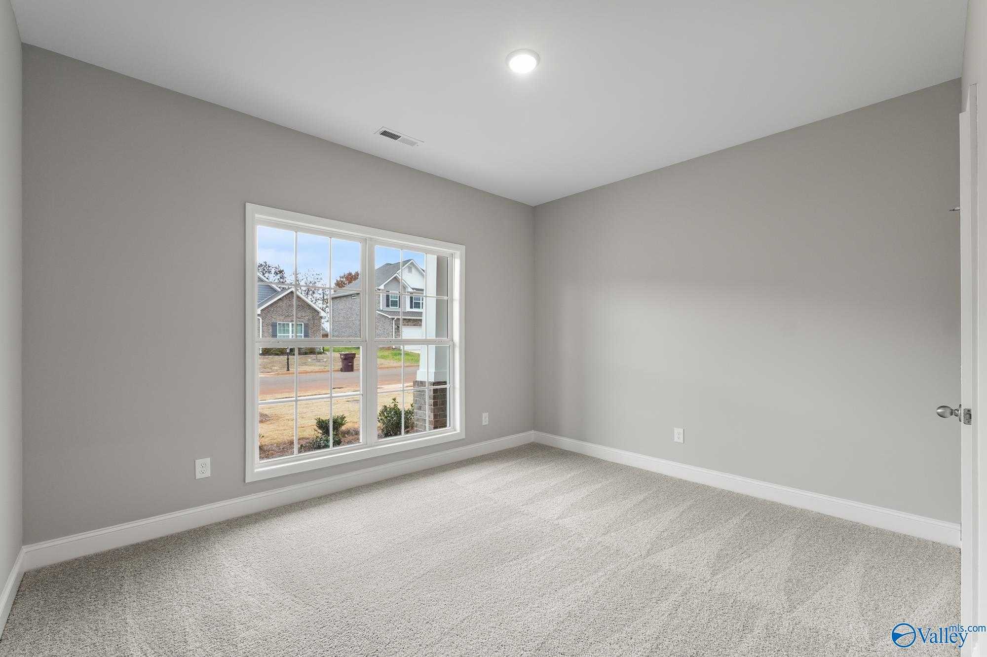 Bright secondary bedroom with gray walls, carpet flooring, and large window view of Ricketts Farm neighborhood in Davidson Homes The Daphne D, Athens, AL