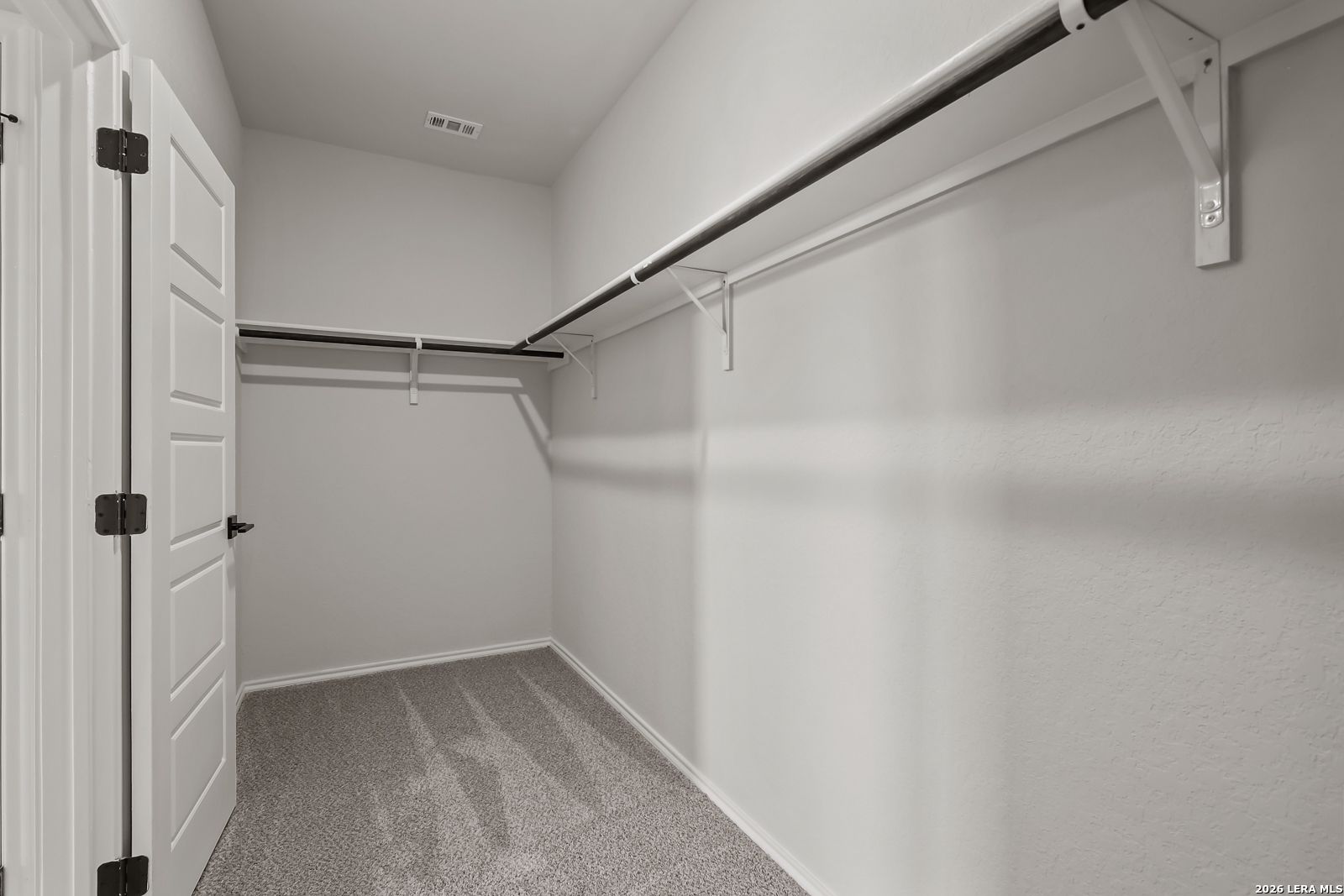 Spacious walk-in closet with double hanging rods, neutral walls, and carpet floor in Davidson Homes The Daphne H, Seguin, Texas