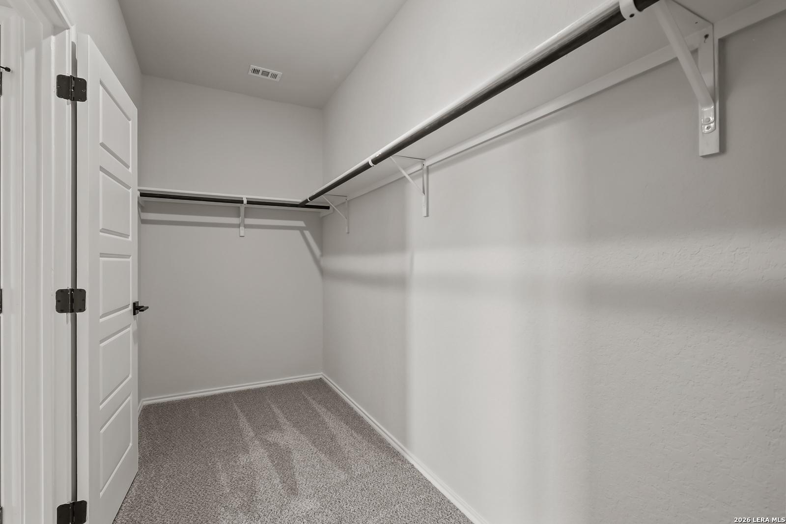 Spacious walk-in closet with double hanging rods, neutral walls, and carpet floor in Davidson Homes The Daphne H, Seguin, Texas