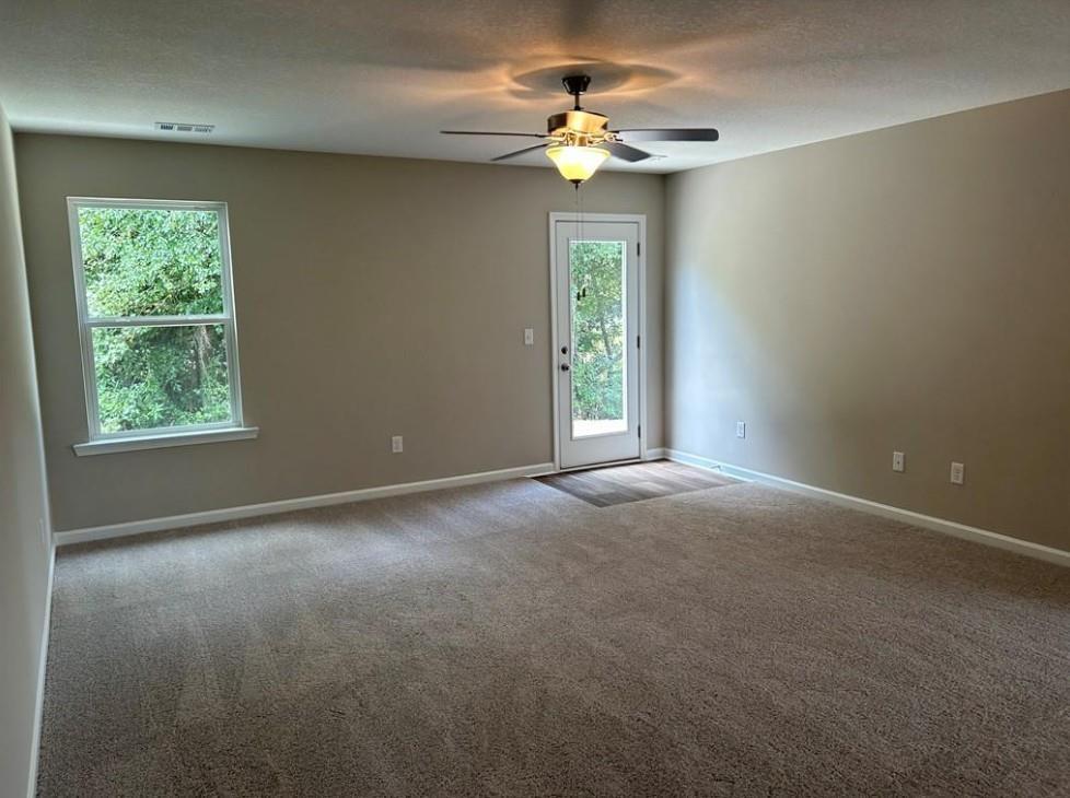 Bright bedroom with ceiling fan, large windows overlooking trees, and glass patio door in Davidson Homes The Washington, Phenix City, Alabama