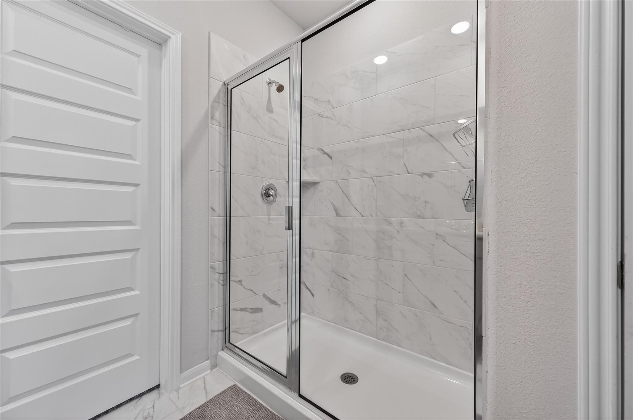 Elegant frameless glass shower with white subway tiles in The Brazos E by Davidson Homes, Magnolia Texas