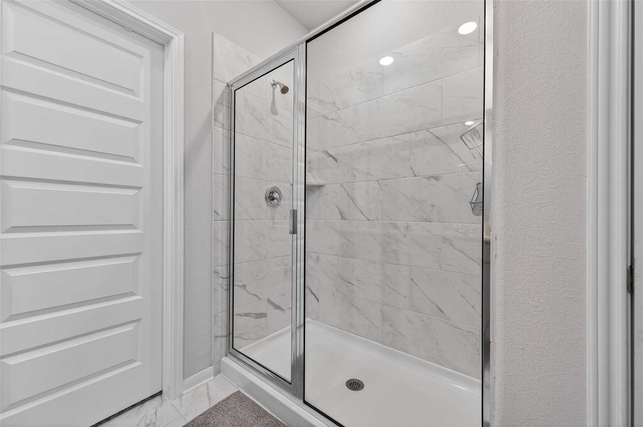 Elegant frameless glass shower with white subway tiles in The Brazos E by Davidson Homes, Magnolia Texas