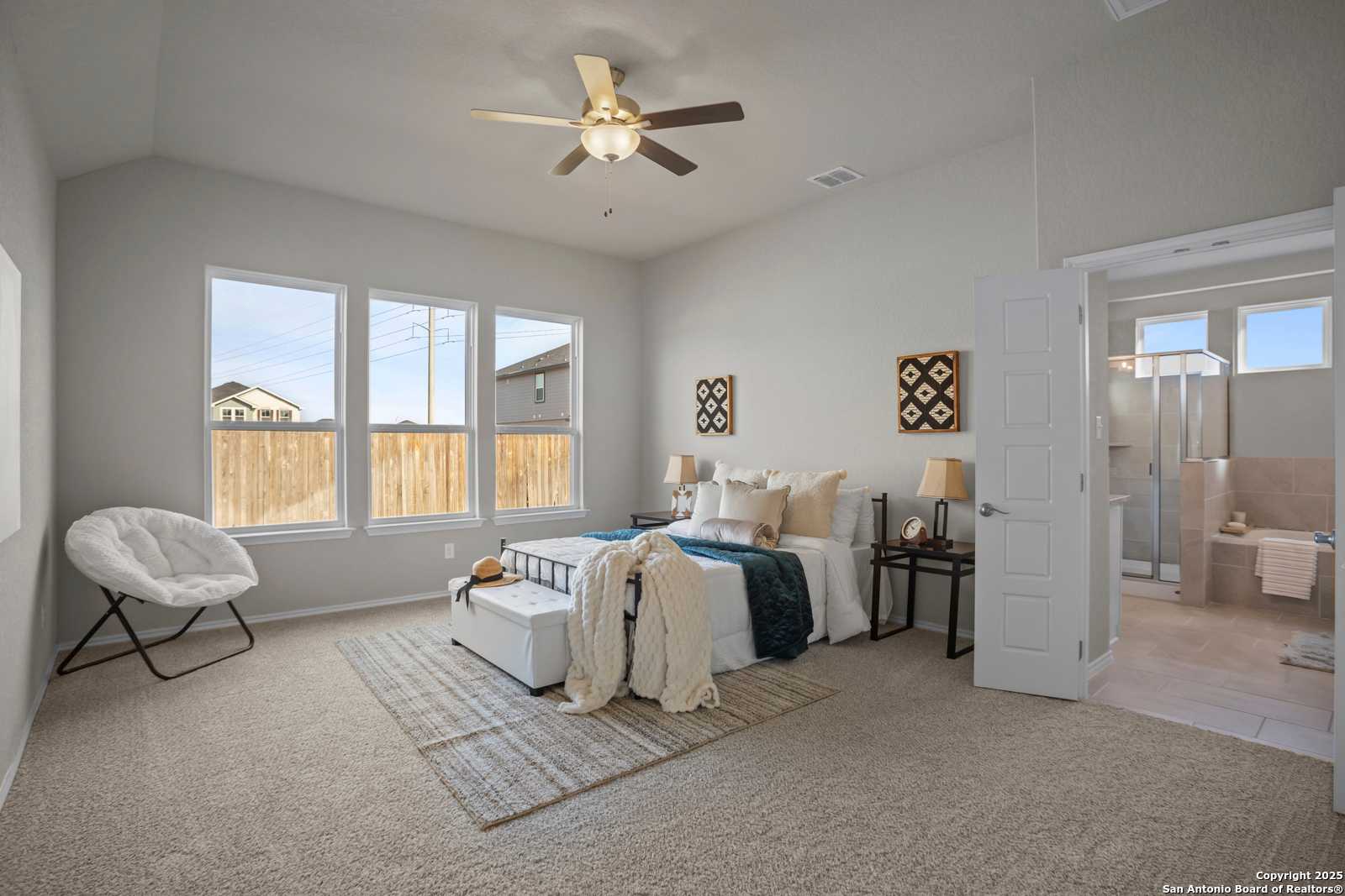 Spacious master bedroom with ceiling fan, large windows, plush bed, and en-suite bath in Davidson Homes The Collin B, Seguin Texas
