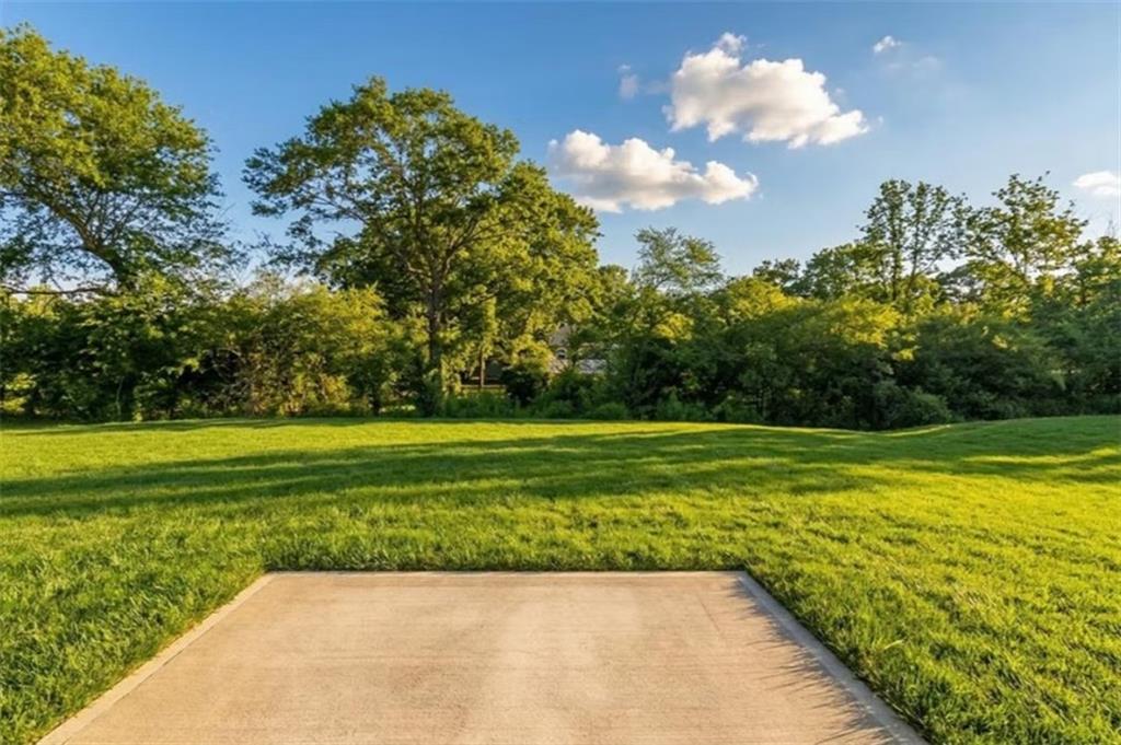 Expansive green lawn with concrete patio slab amid lush trees and shrubs under blue sky in Cedar Farms, Winder, Georgia