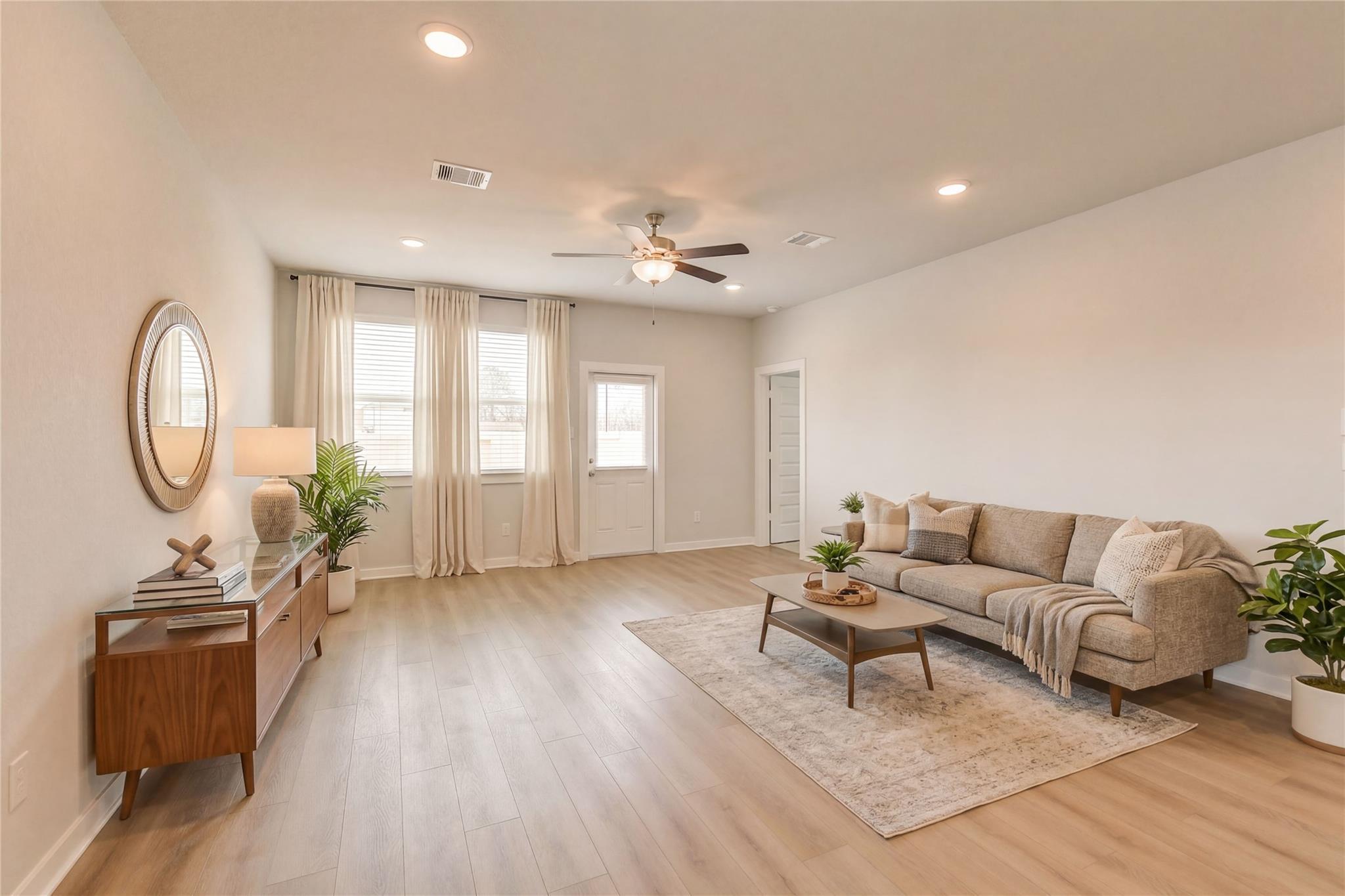 Spacious living room with beige sectional sofa, wooden coffee table, potted plants, ceiling fan in Davidson Homes The Brazos E, Cleveland, Texas