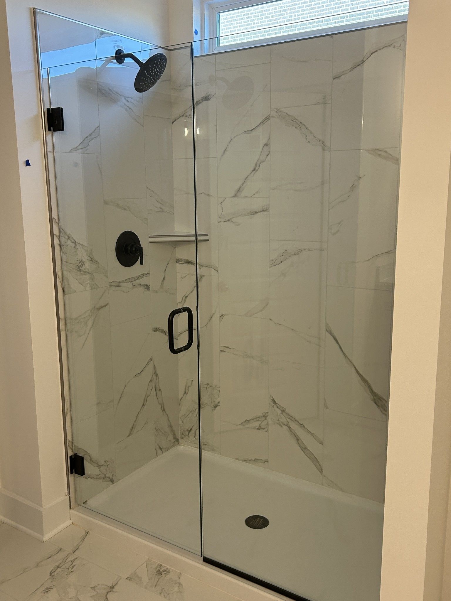 Modern frameless glass shower with white marble tiles, black rain showerhead in master bath of Davidson Homes The Ridgeport E, Mt. Juliet, TN