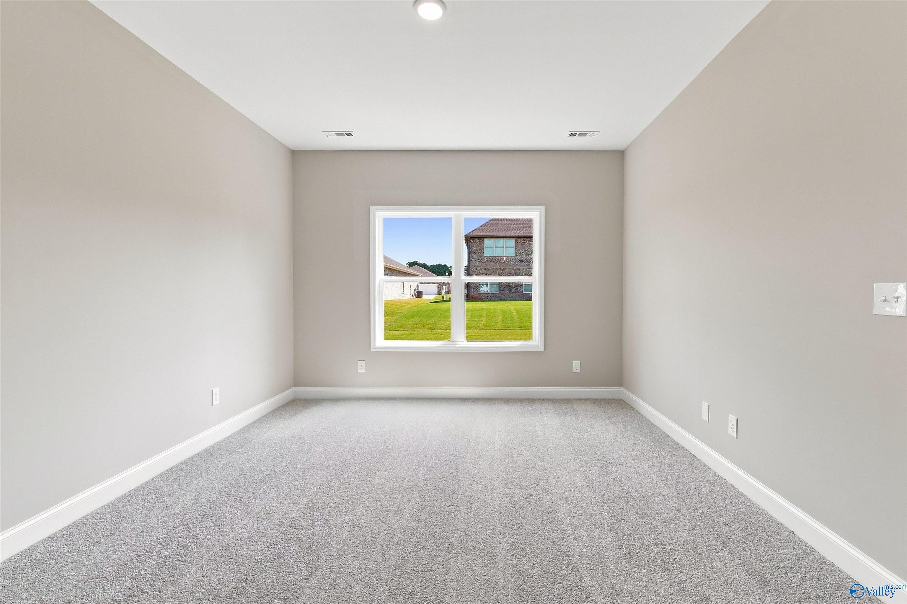 Bright neutral bedroom with plush gray carpet and window view in Davidson Homes The Franklin C, Wood Trail, Toney, Alabama