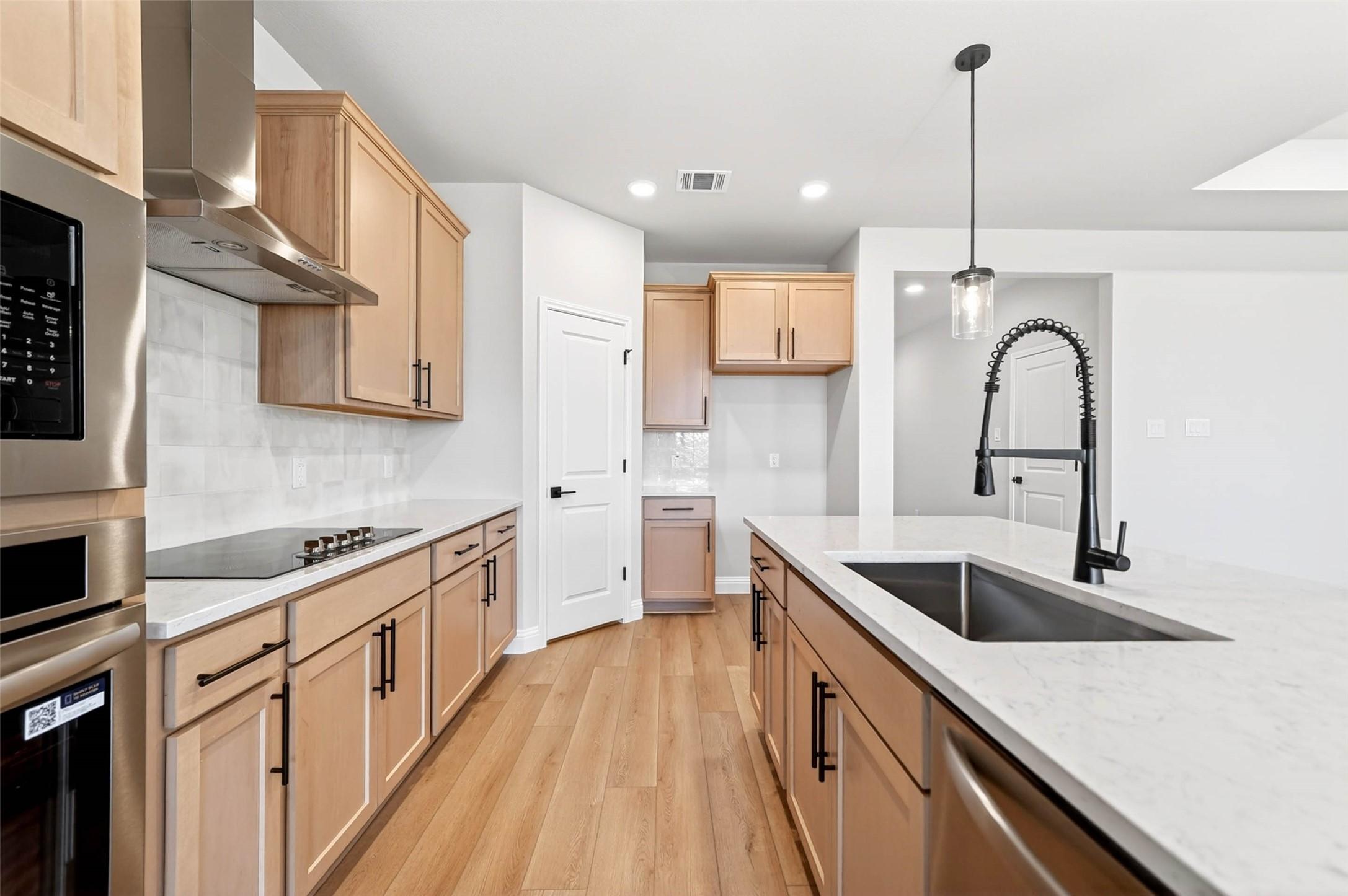 Modern kitchen with light wood cabinets, white countertops, and large island in The Holly C home, Parks at Foster Crossing.