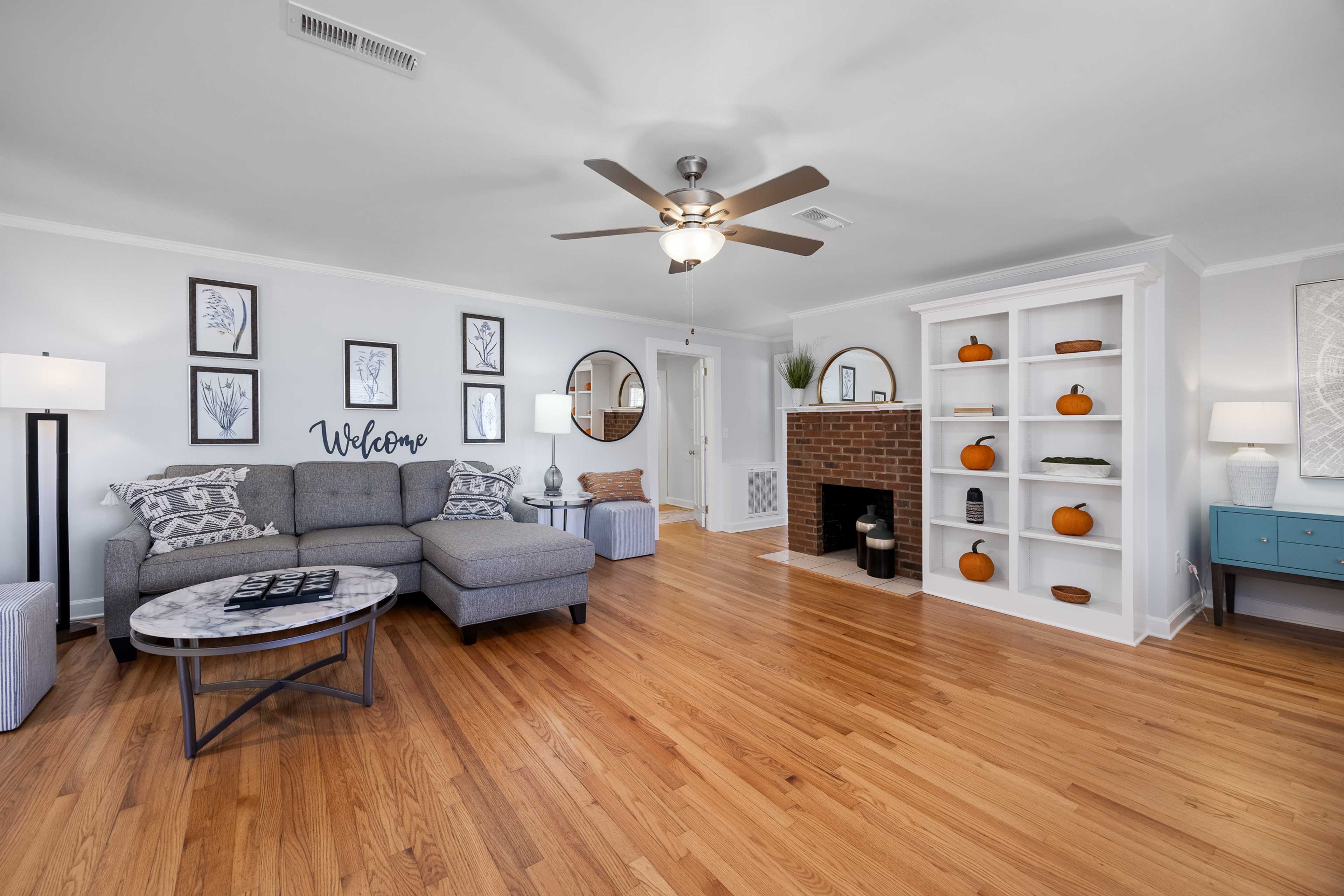 Cozy living room at Stagecoach Corner in Mebane NC with gray sectional sofa, brick fireplace, hardwood floors, and fall decor