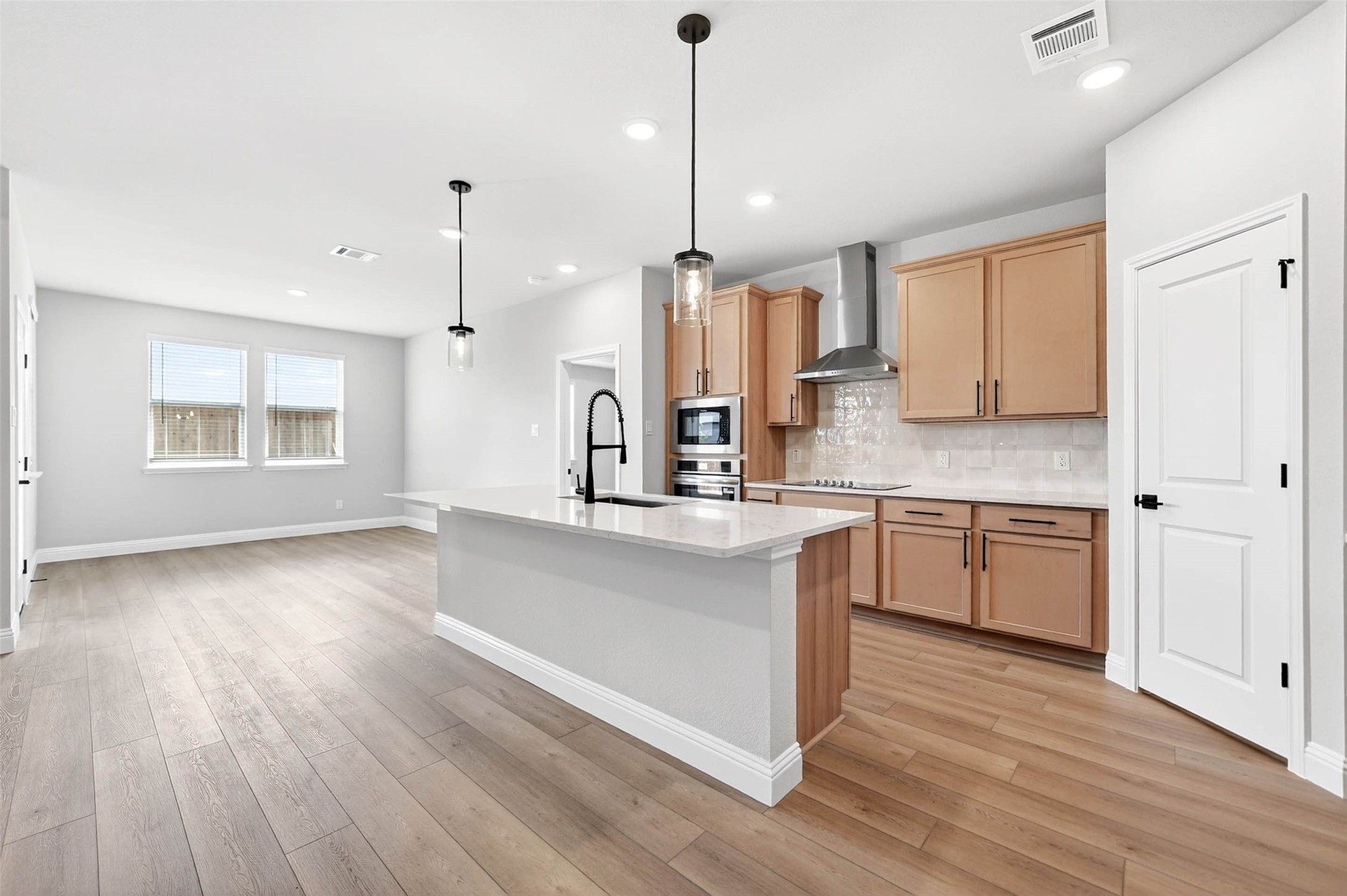 Modern kitchen with light wood cabinets, quartz island, and pendant lighting in The Holly C home at Parks at Foster Crossing.