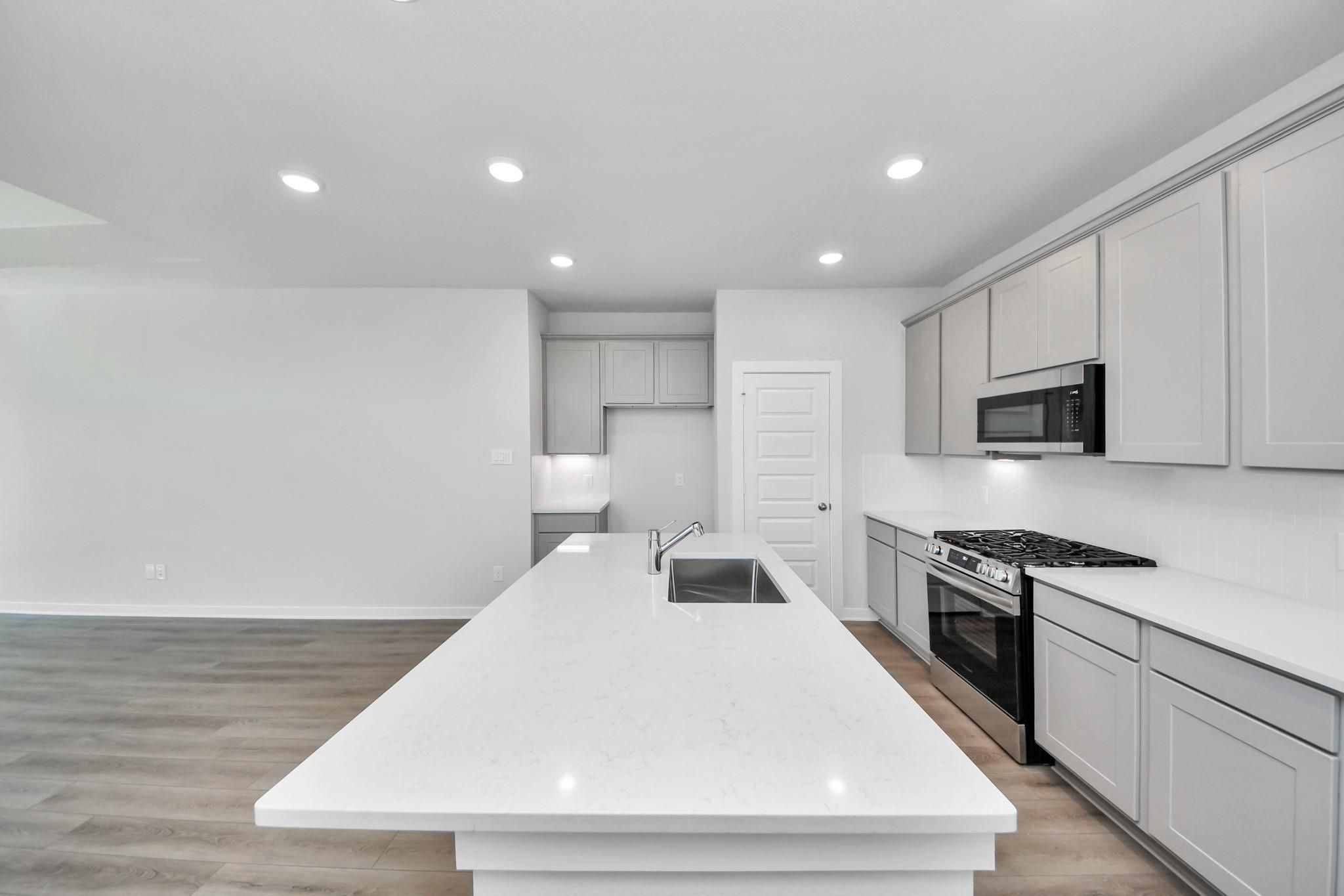 Modern kitchen with white quartz island, gray cabinets, and stainless appliances in The Colorado G home in Emberly, Beasley.