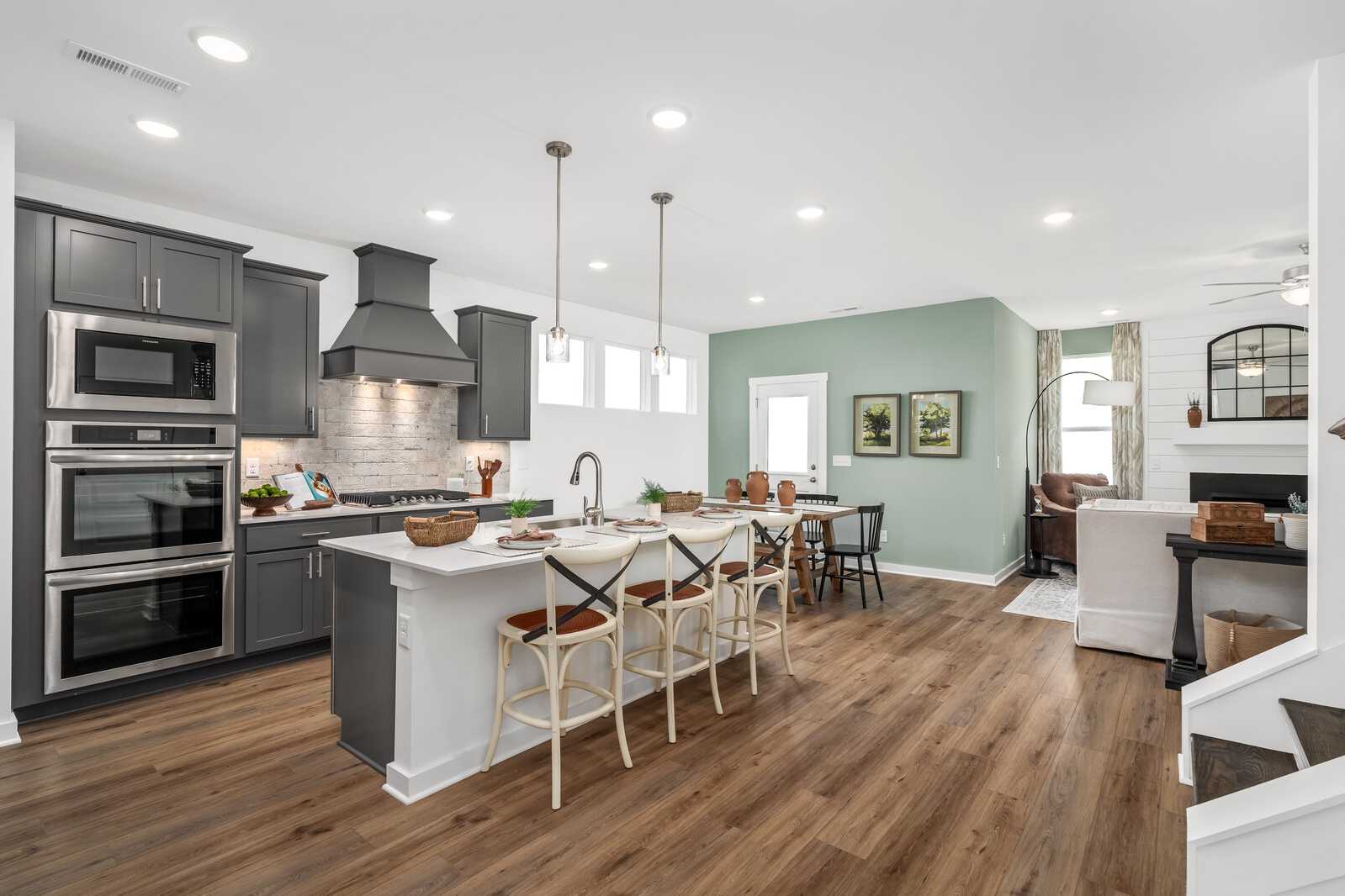 Open-concept kitchen at Calista Farms in White House TN with gray cabinets, large white island, hardwood floors and dining nook