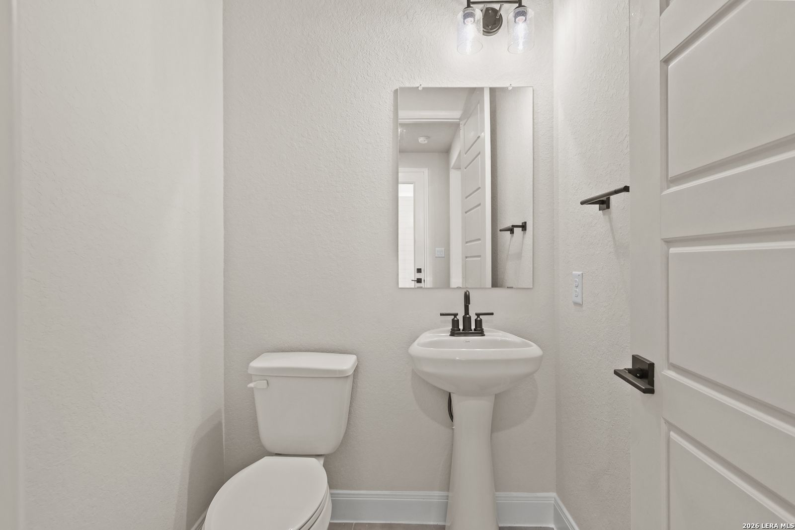 Half-bathroom with pedestal sink and mirror in The Summerlin B floor plan by Davidson Homes in Potranco Oaks, Castroville.