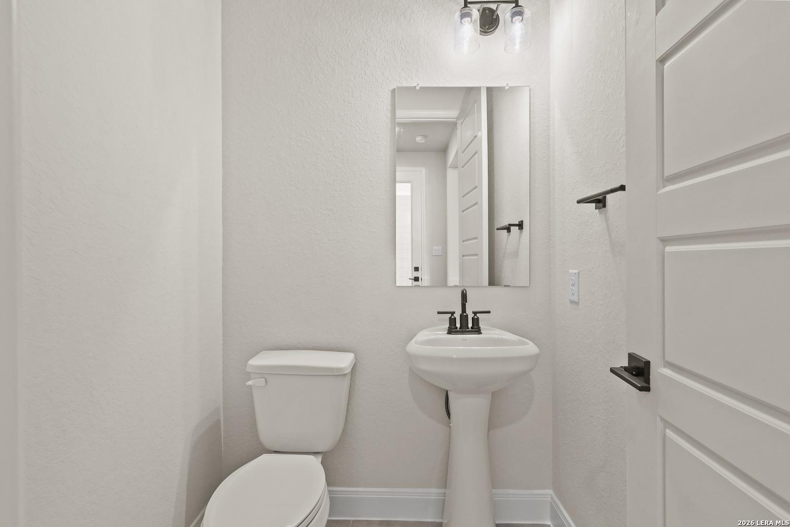 Half-bathroom with pedestal sink and mirror in The Summerlin B floor plan by Davidson Homes in Potranco Oaks, Castroville.