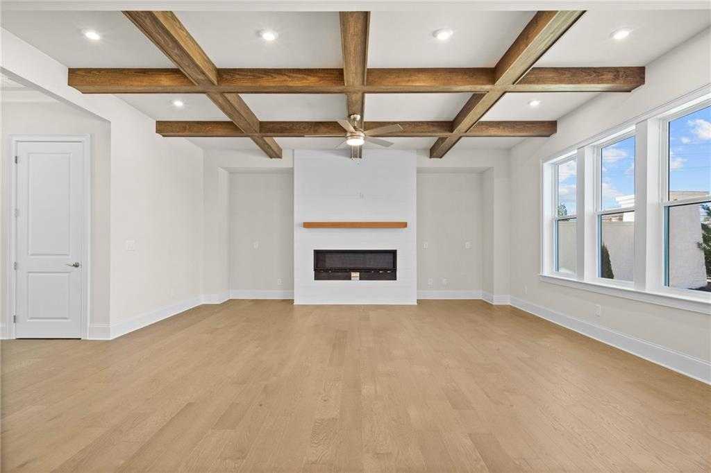 Spacious living room with exposed wood beam ceiling, hardwood floors, modern white fireplace, and large windows in Davidson Homes The Arlington A, East Cobb