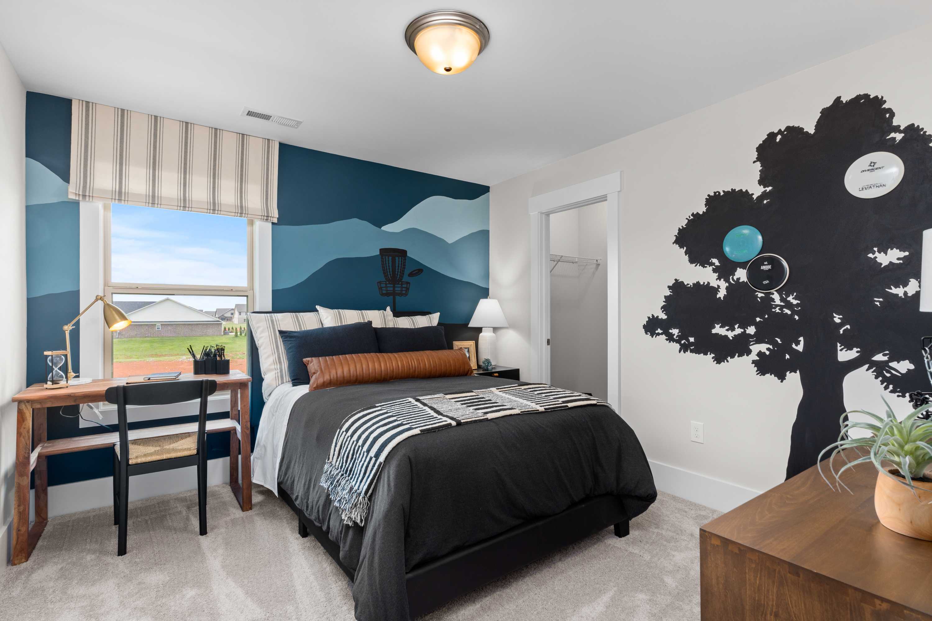 Youthful bedroom in The Chelsea B with navy walls, mountain mural, skateboard silhouette, cozy bed, wooden desk, and window view