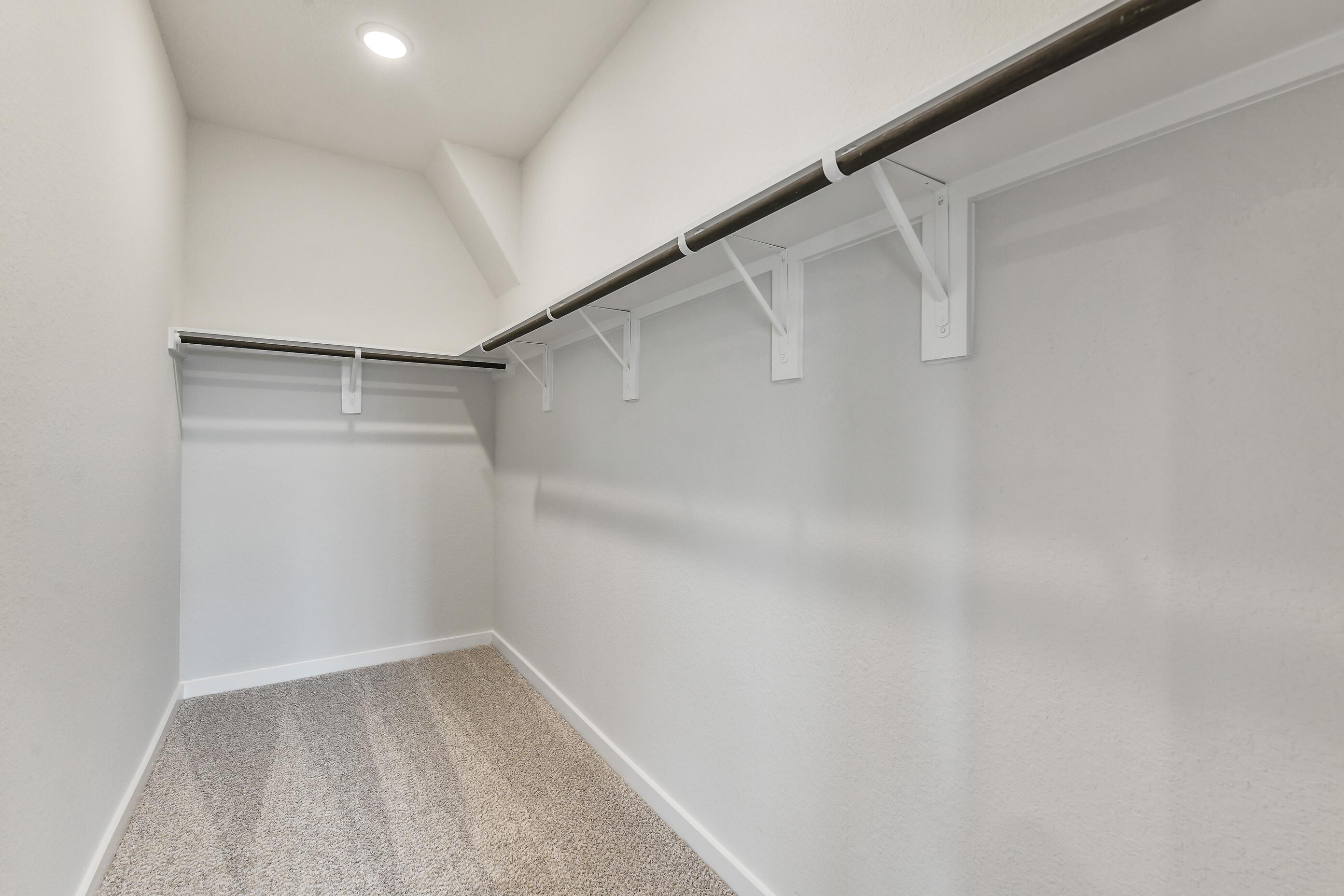 Spacious walk-in closet with white built-in shelves and hanging rods on beige carpet in Davidson Homes The Colorado G, Magnolia, Texas