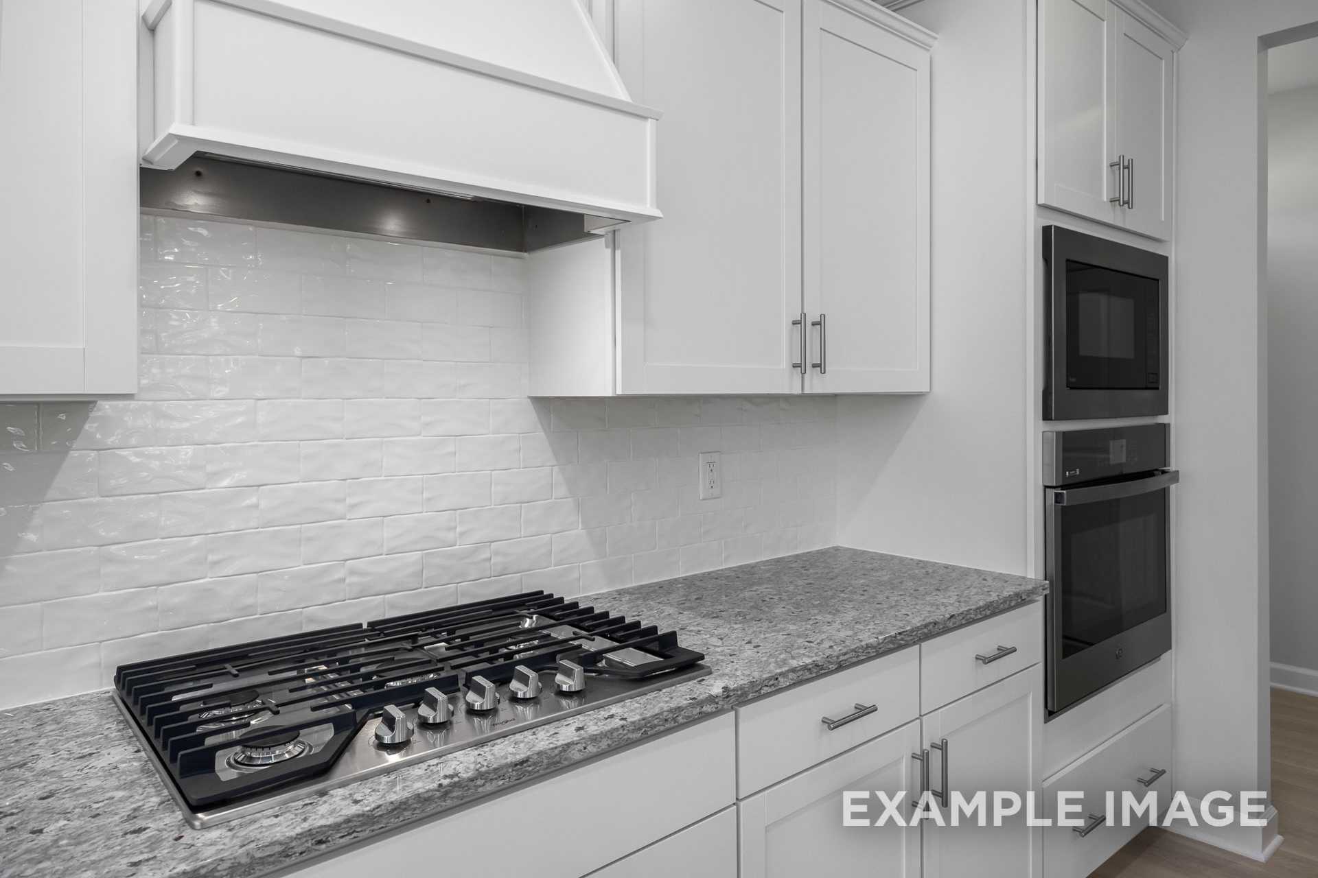 Modern kitchen in The Gavin C home design with white shaker cabinets, subway tile backsplash, granite counters, and gas range