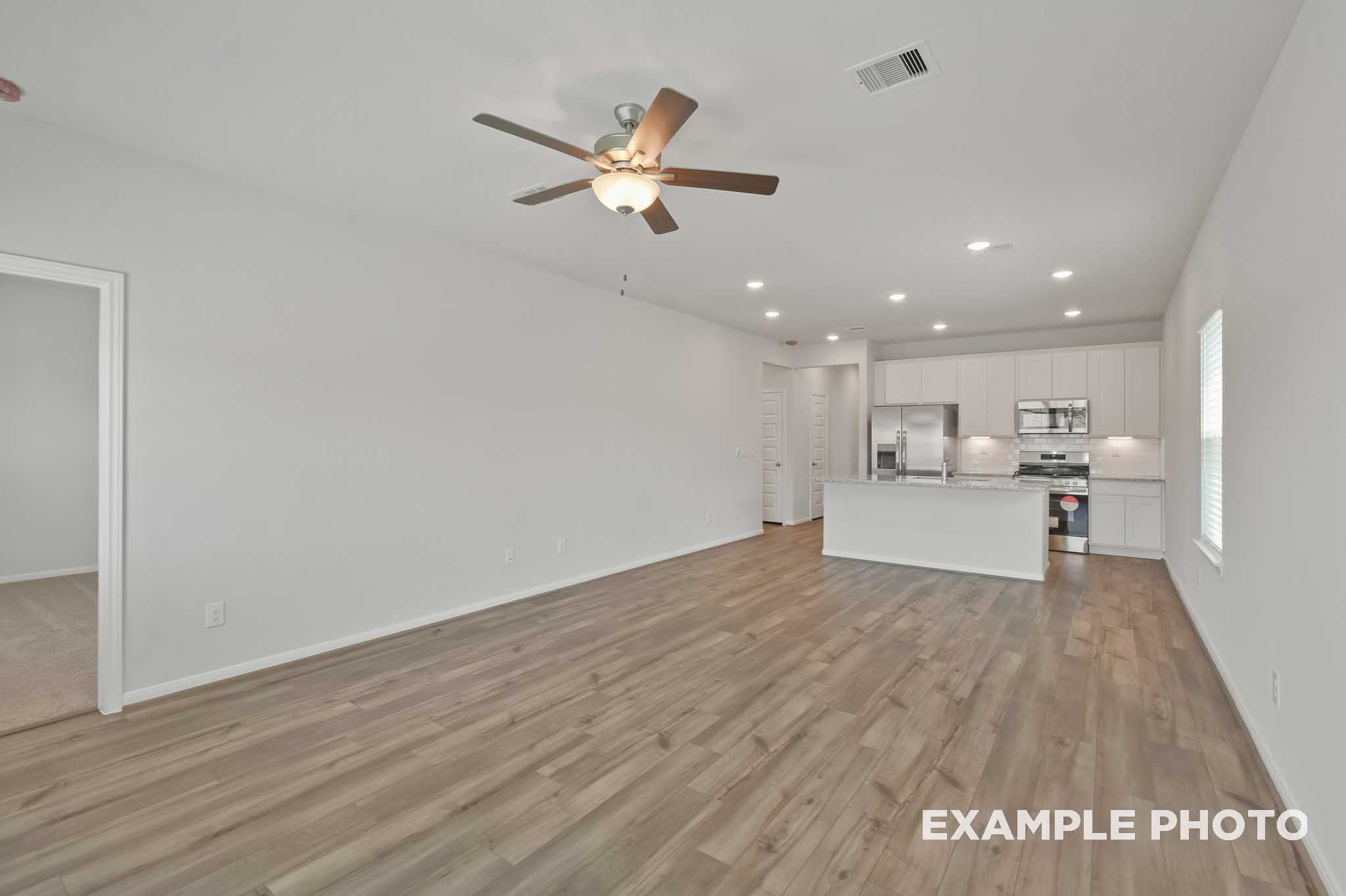 Spacious open-concept kitchen in The Comal floor plan with white cabinetry, large island, stainless appliances, and hardwood floors