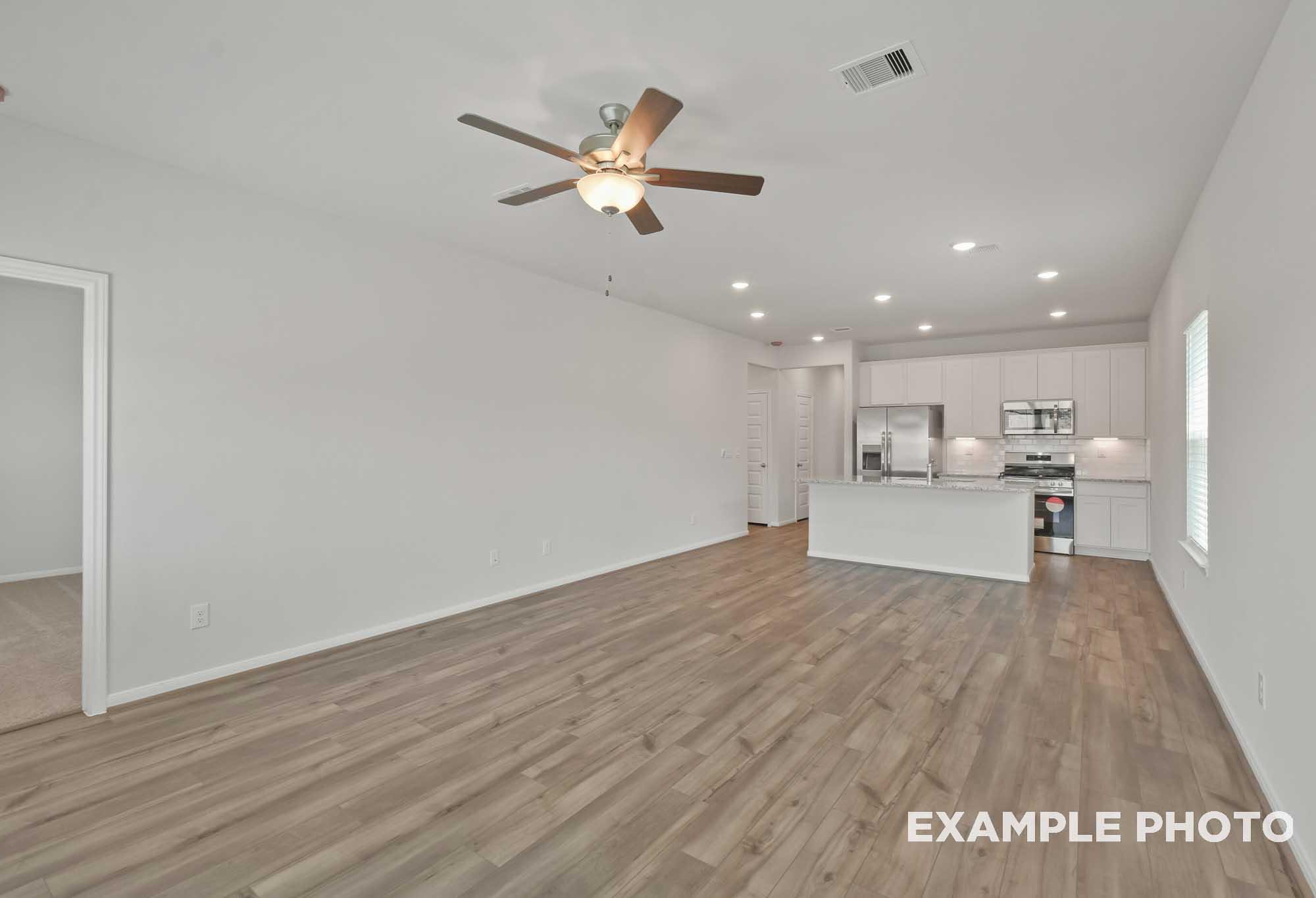 Spacious open-concept kitchen in The Comal floor plan with white cabinetry, large island, stainless appliances, and hardwood floors