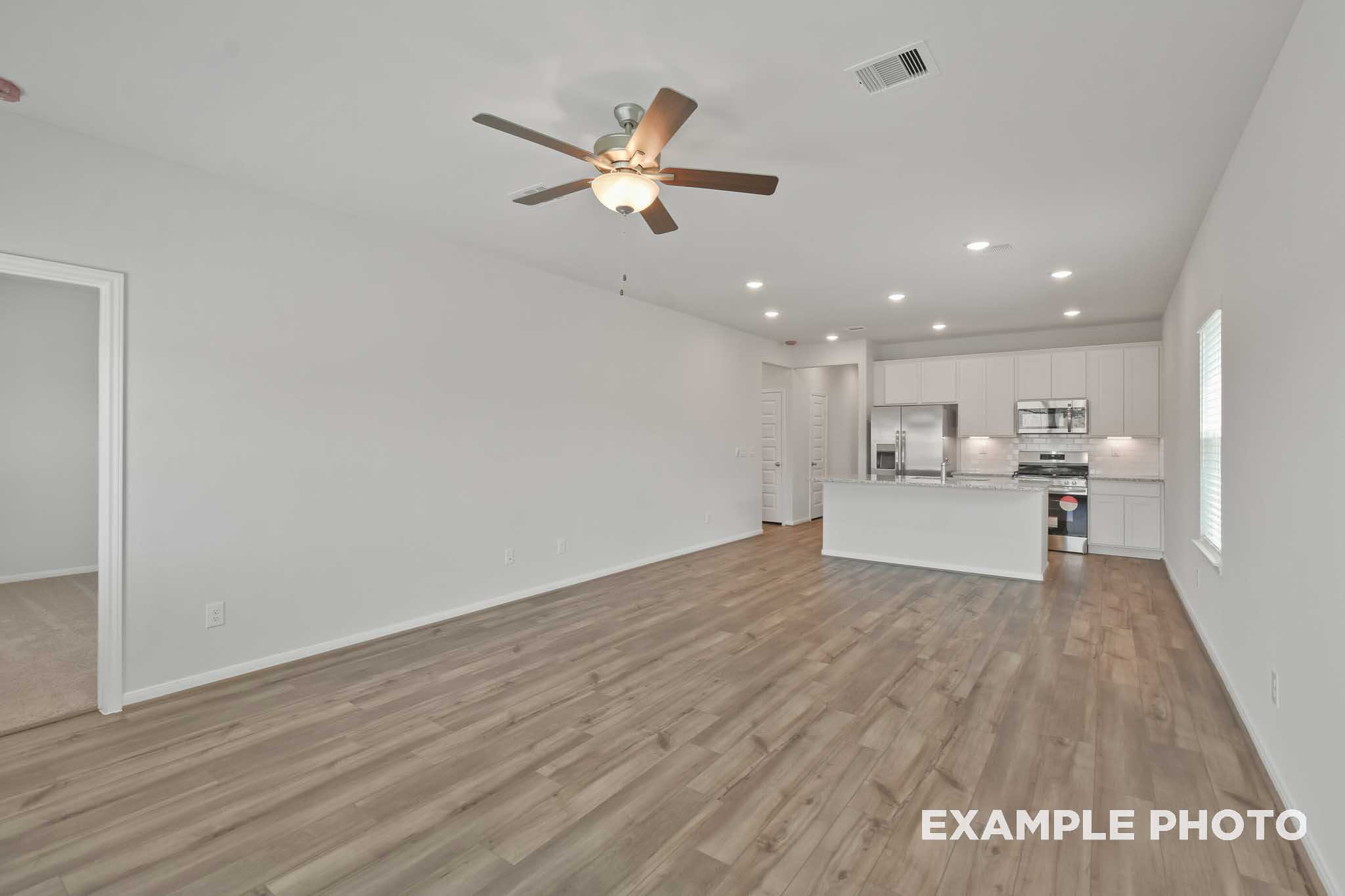 Spacious open-concept kitchen in The Comal floor plan with white cabinetry, large island, stainless appliances, and hardwood floors