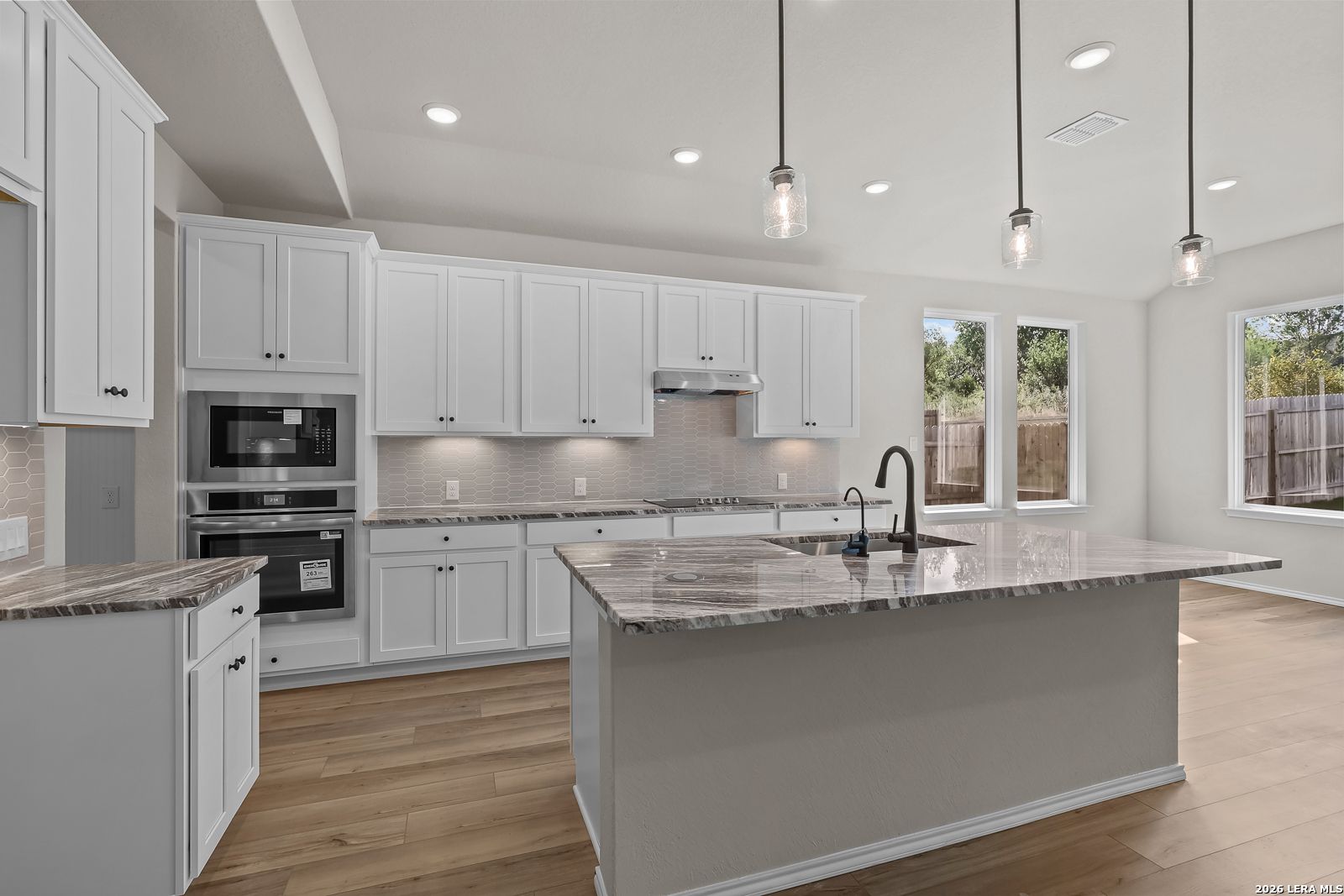 Modern white kitchen with granite island, stainless appliances, and pendant lights in Davidson Homes Sequoia C, San Antonio